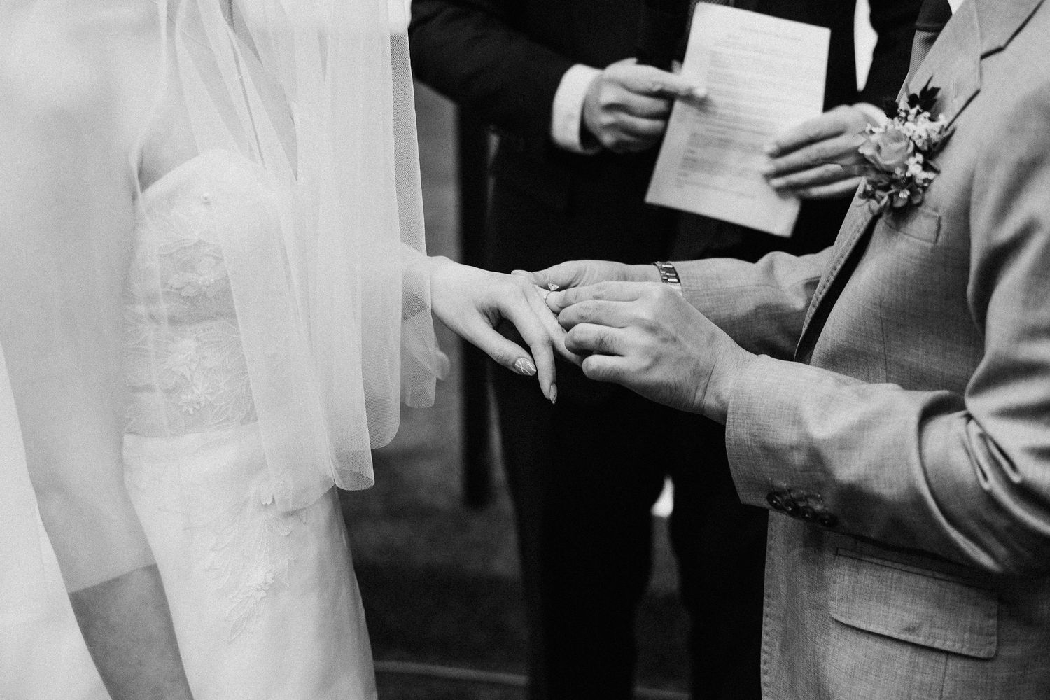 Black and white close-up of hands exchanging rings during wedding ceremony.