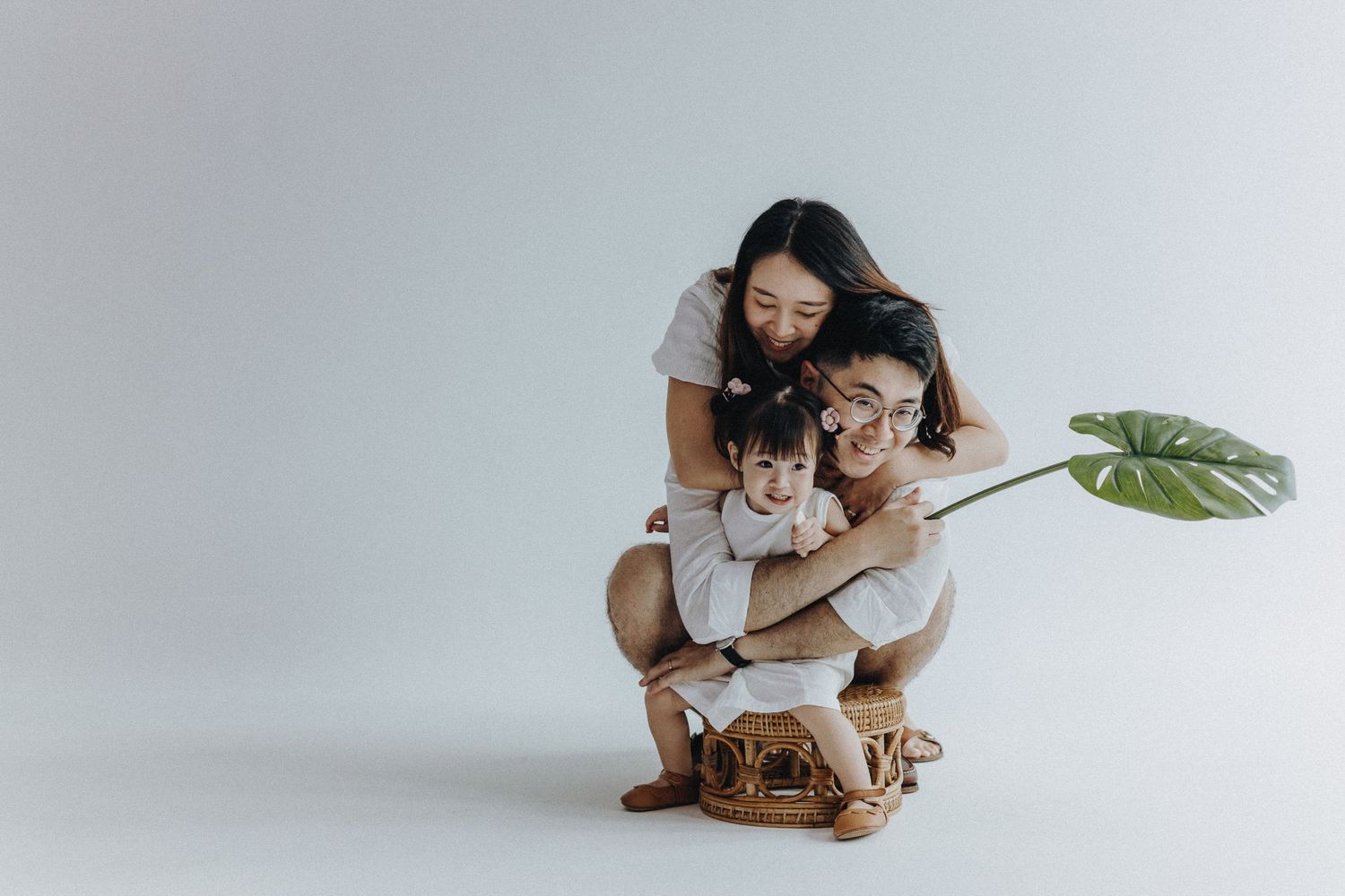 Candid family moments captured in a clean white studio setting with rattan furniture.