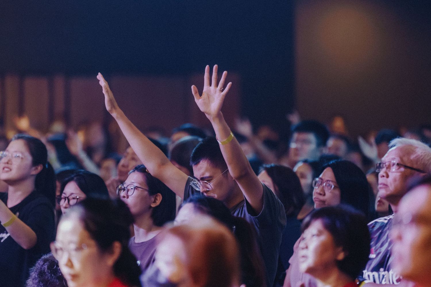 Enthusiastic audience members raise their hands and look upward during a concert performance.