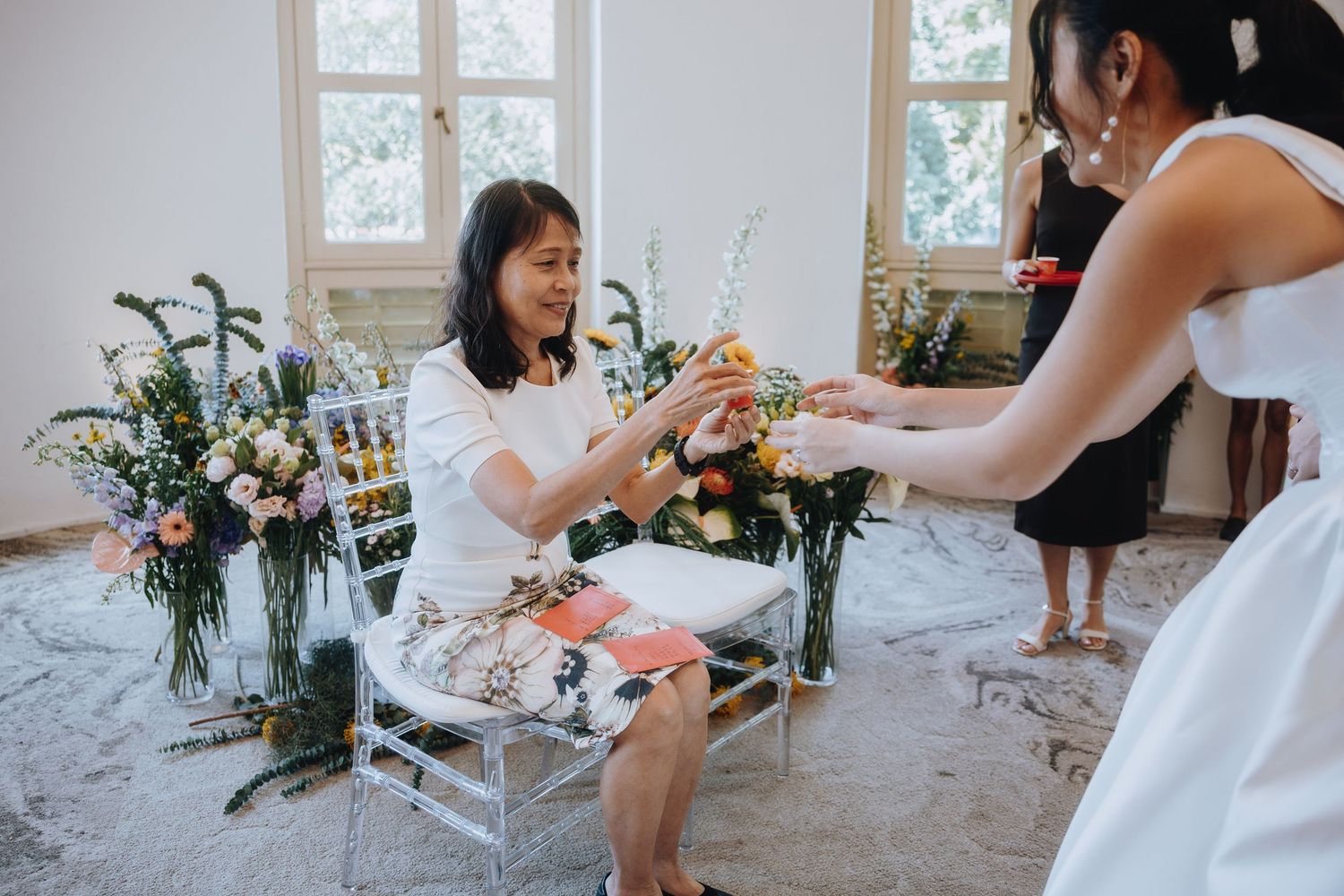 Wedding guest seated in chair receives a gift from bride during reception celebration.