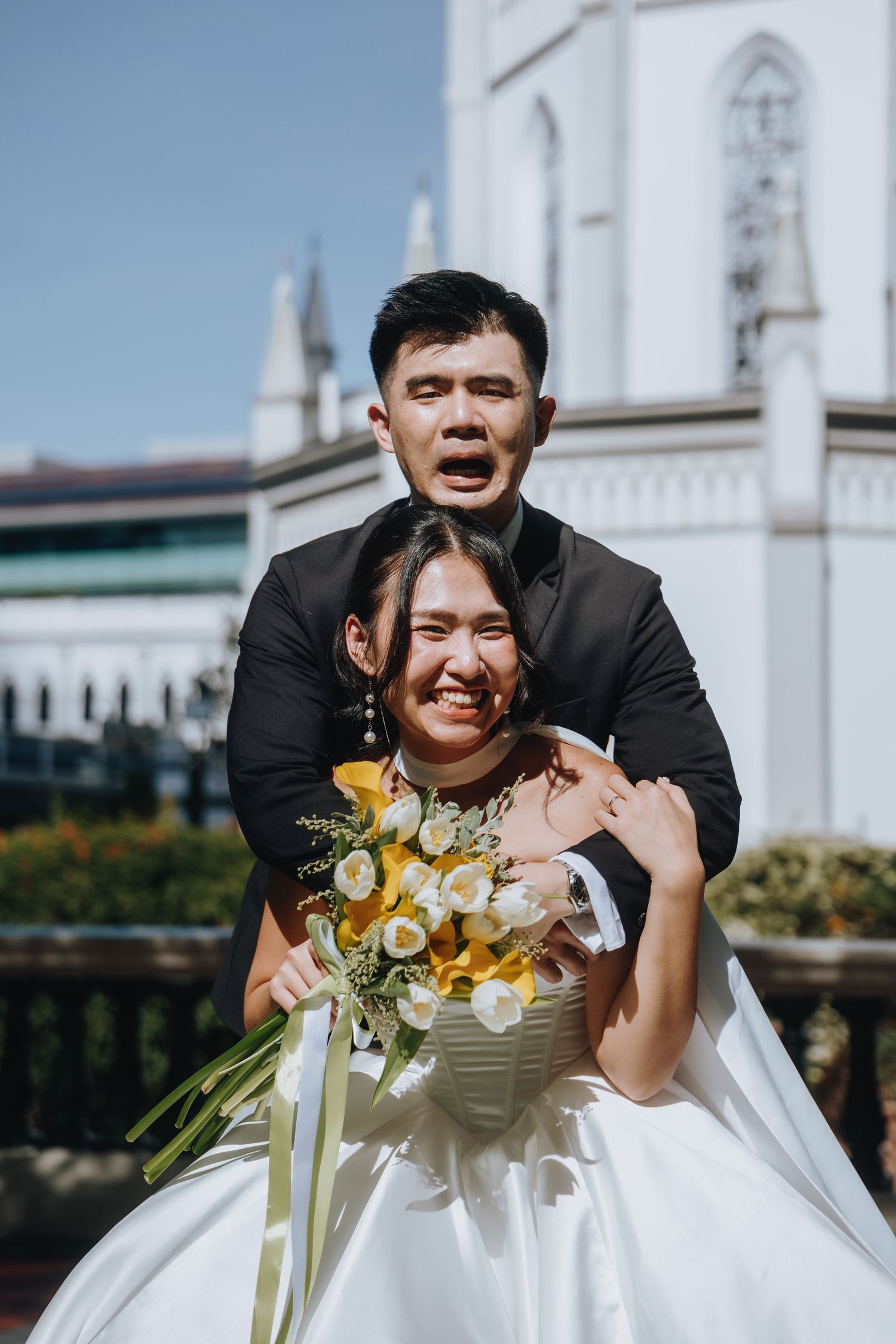 Joyful bride and groom making funny faces outside a white church on wedding day.