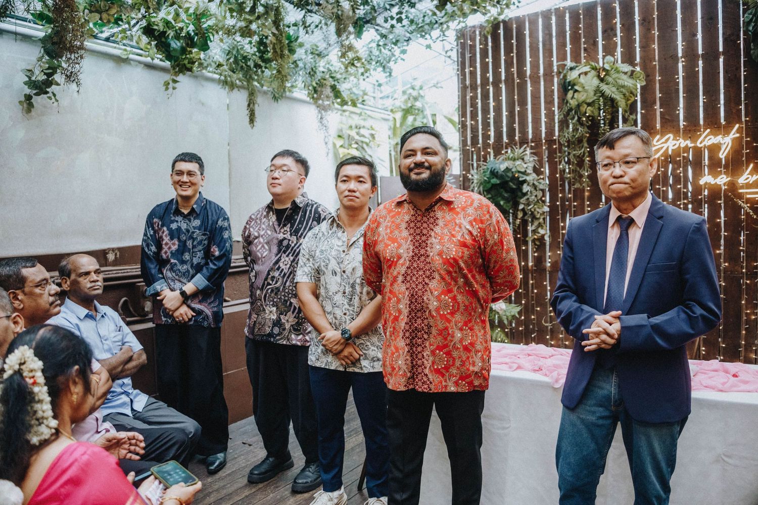 Group of men in batik shirts posing together at outdoor wedding reception.