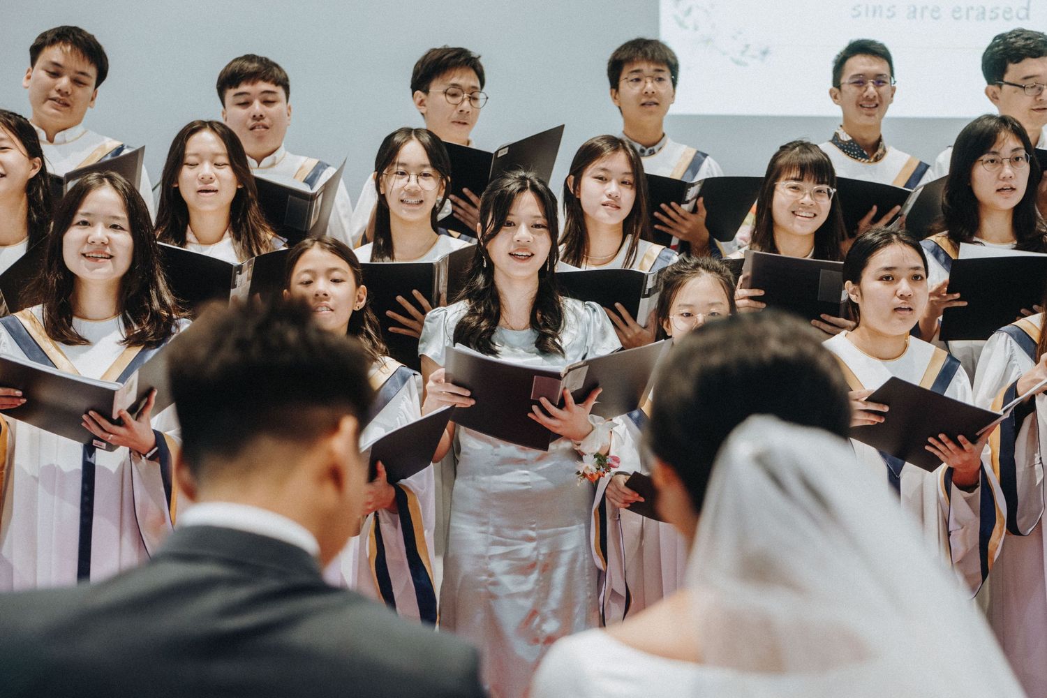 Wedding choir in robes singing from hymnals during a church ceremony.