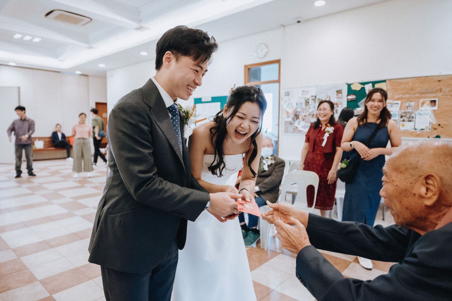 Newlyweds receive red envelope gift from elderly guest at wedding reception.