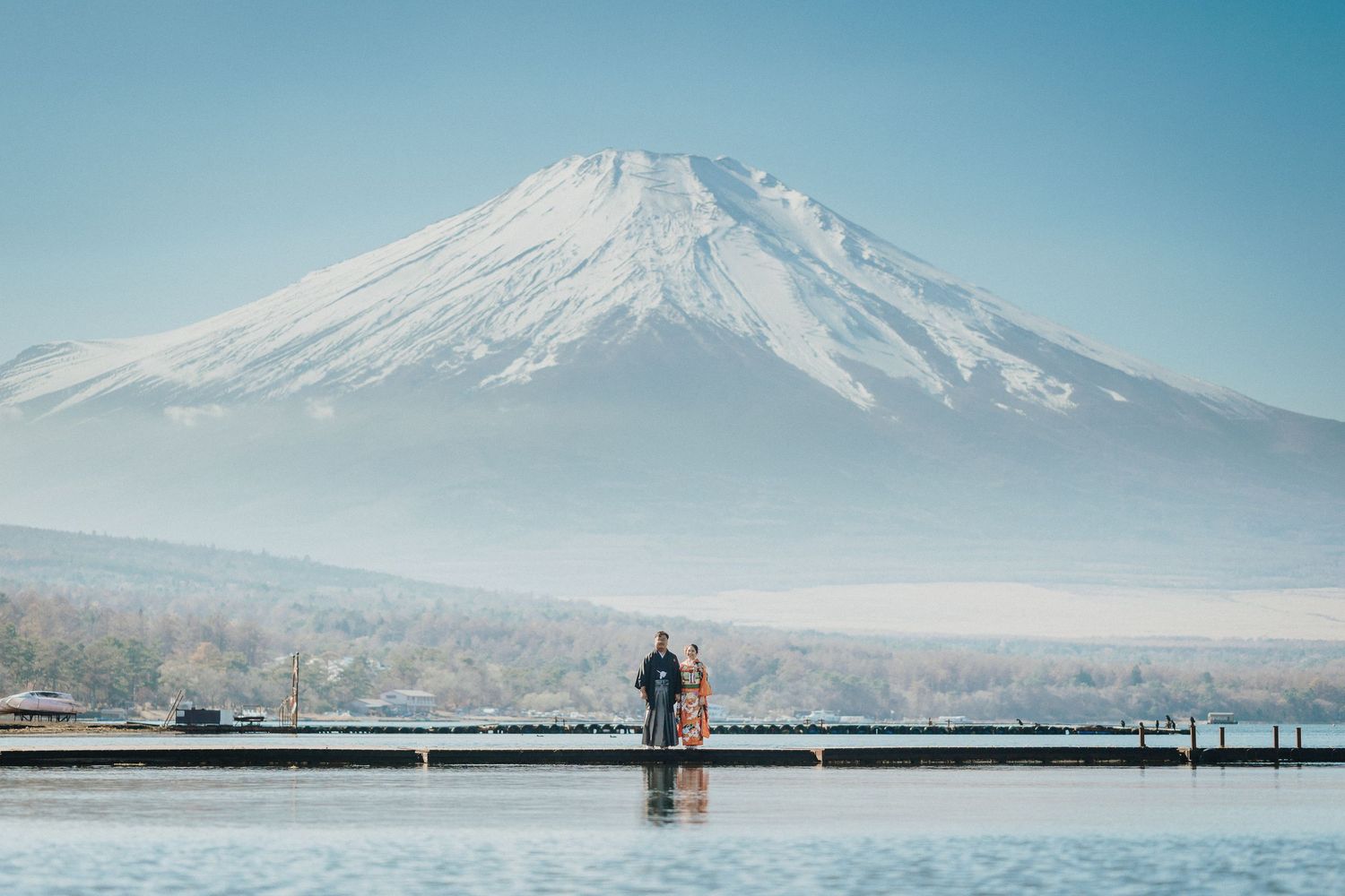 A couple stands silhouetted against Mount Fuji's snow-capped peak on a misty morning.