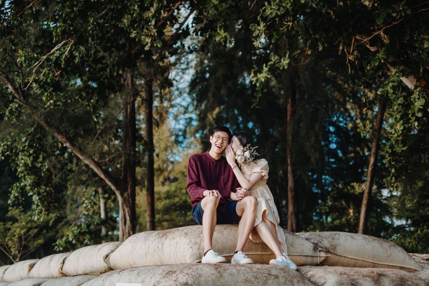 Romantic beach photoshoot with couple sitting on sandbags near the ocean.