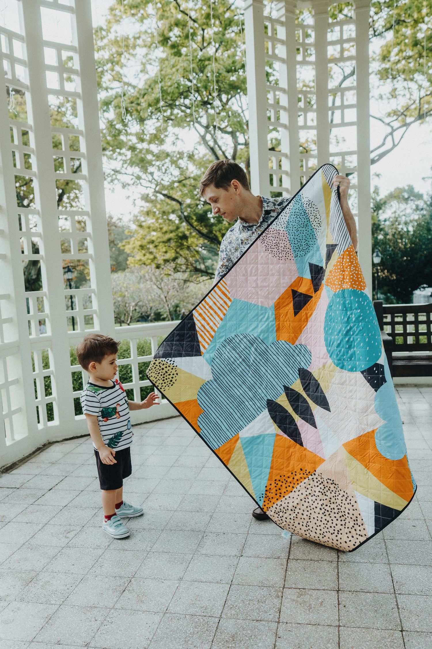 Modern geometric patchwork quilt in turquoise, orange and white displayed in outdoor gazebo.