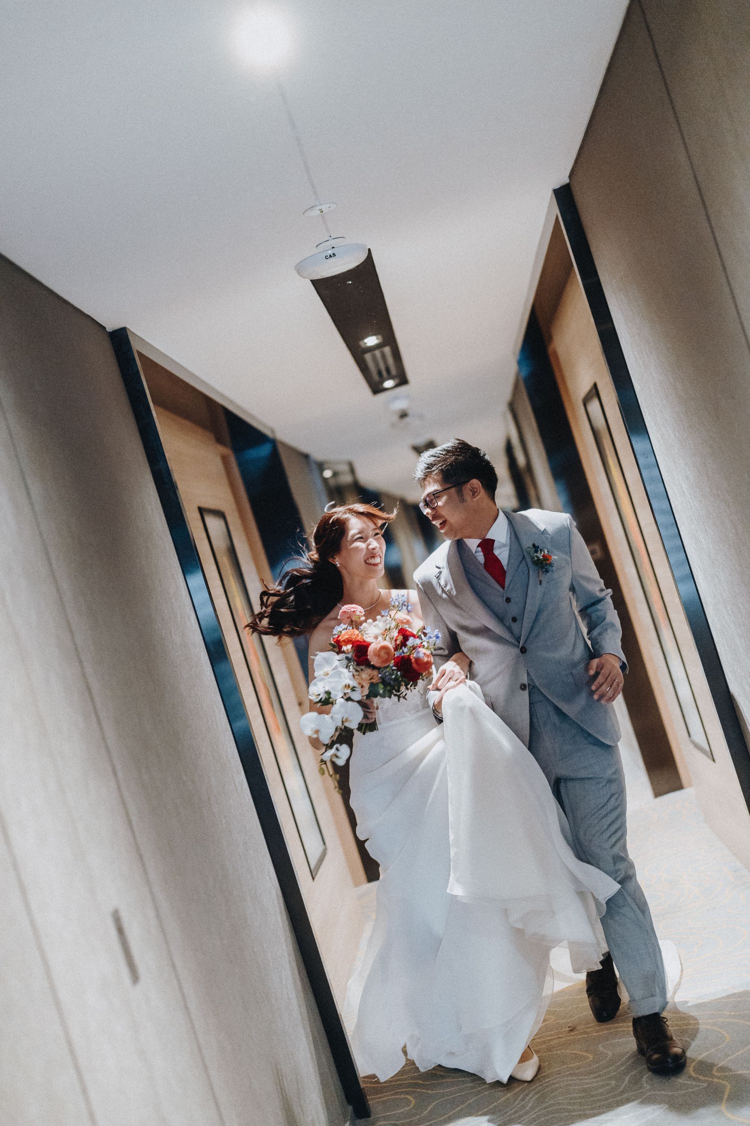 Wedding couple playfully poses in a hallway, with the bride holding a colorful bouquet.