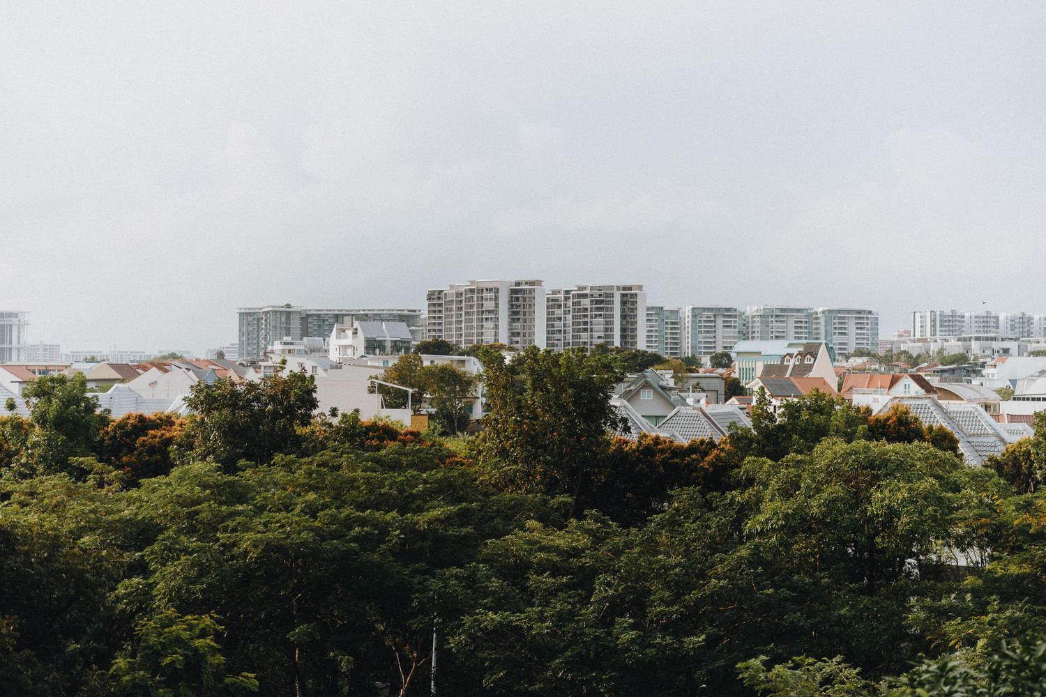 Urban landscape showing high-rise buildings and residential areas with lush greenery in foreground.