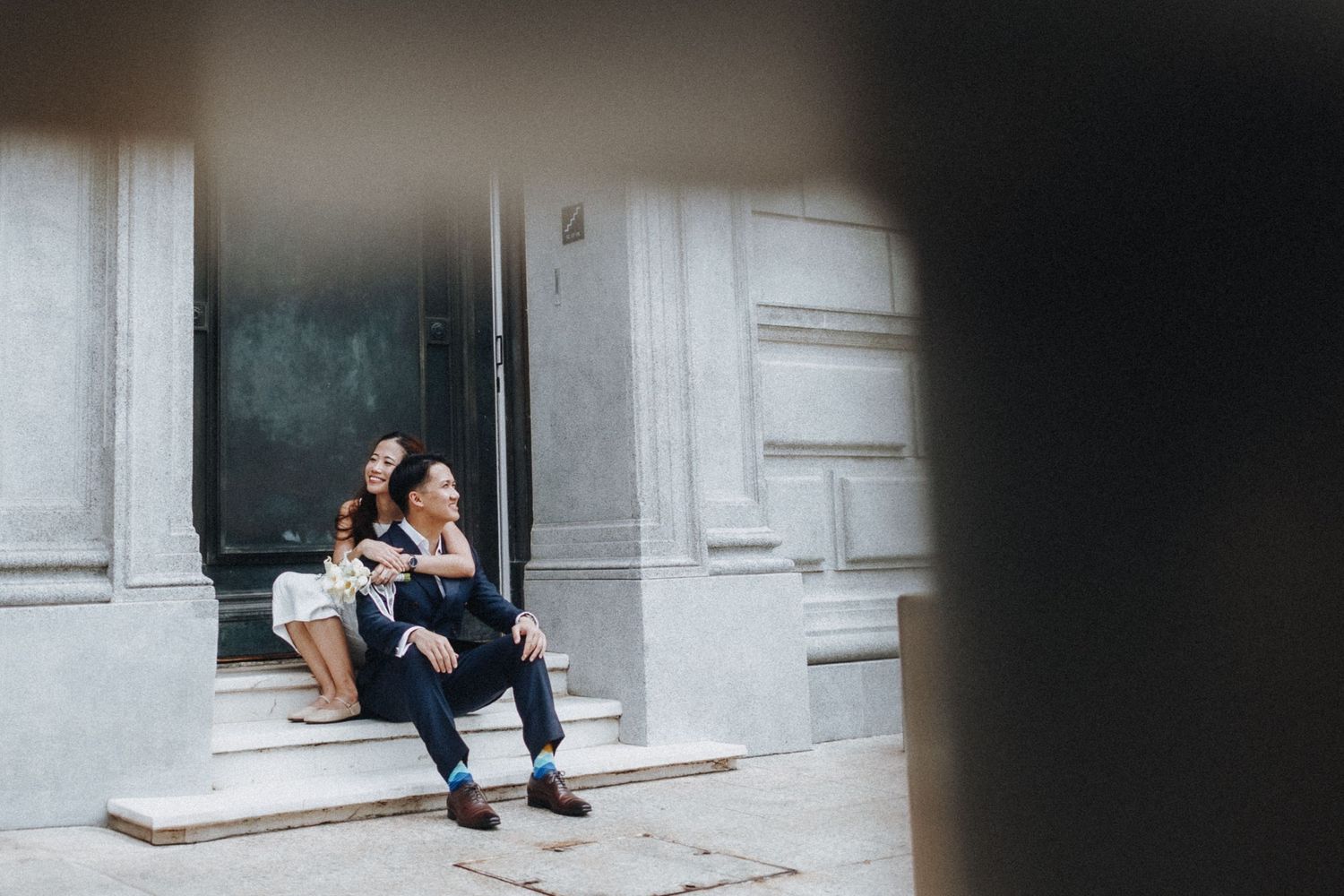 Couple resting on concrete steps of a modern building entrance.