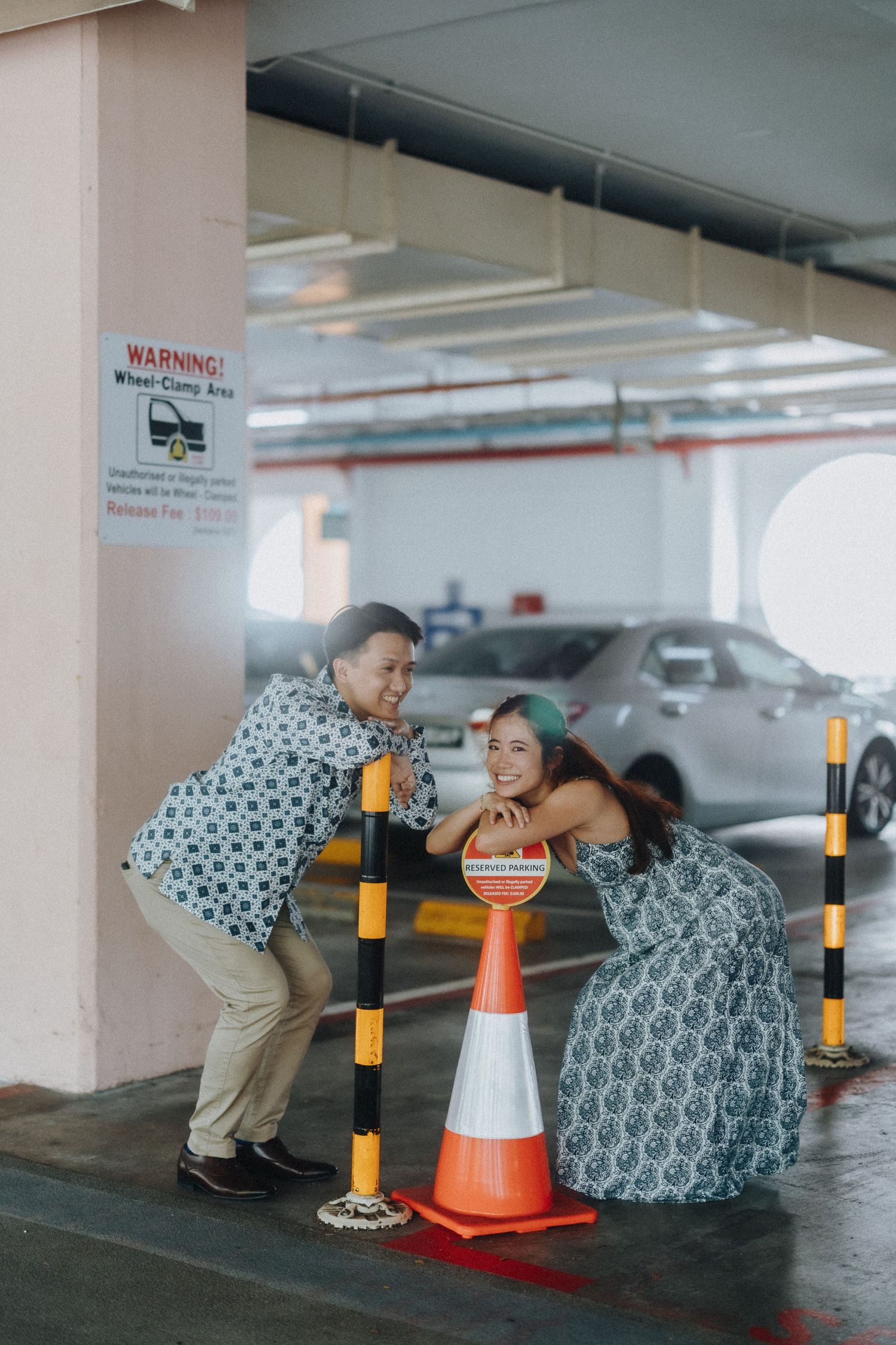 A playful couple in matching patterned outfits poses with a traffic cone in an indoor parking garage.