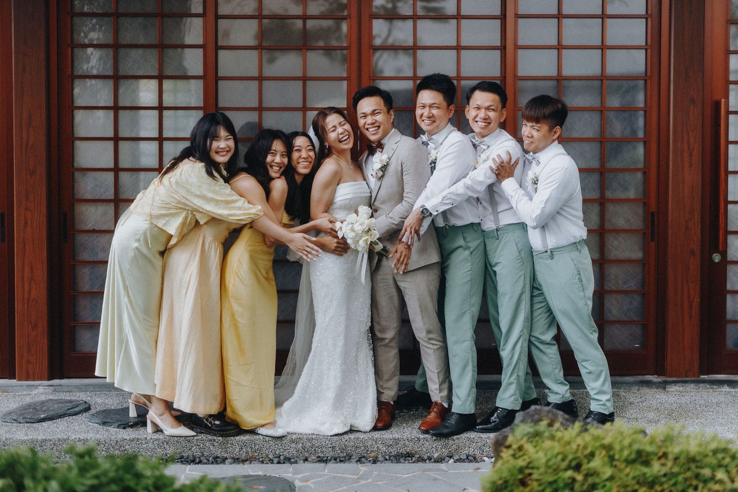 Wedding party in pastels and white poses together on traditional Japanese architecture porch.
