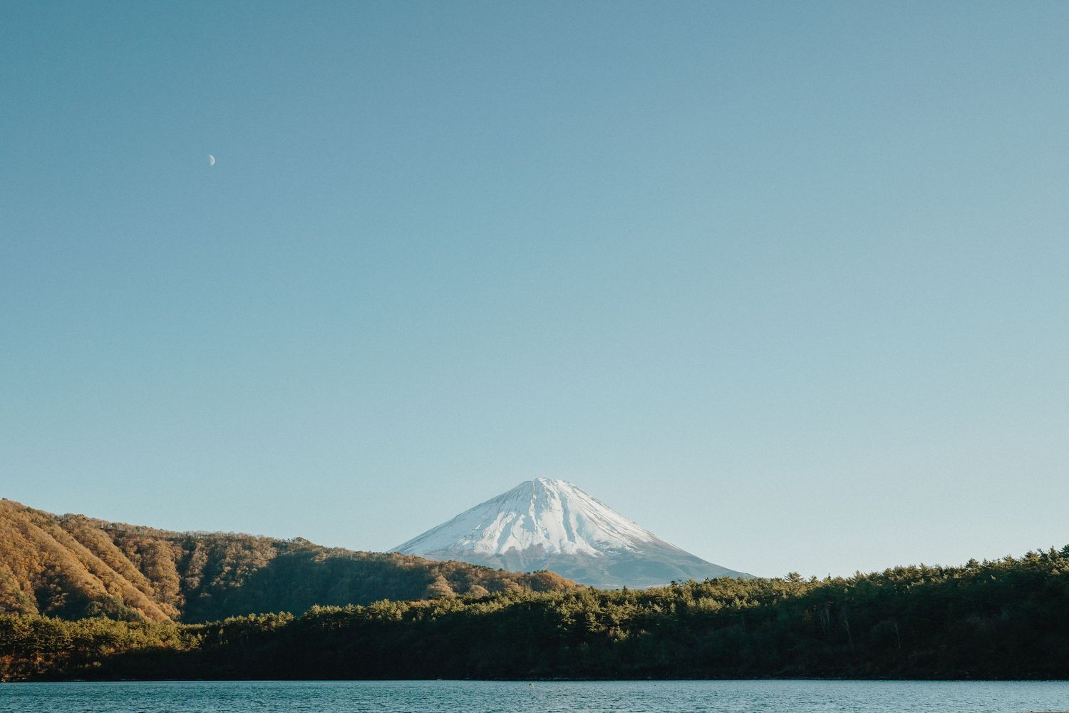 Scenic view of Mount Fuji rising above a lake under pristine blue skies.