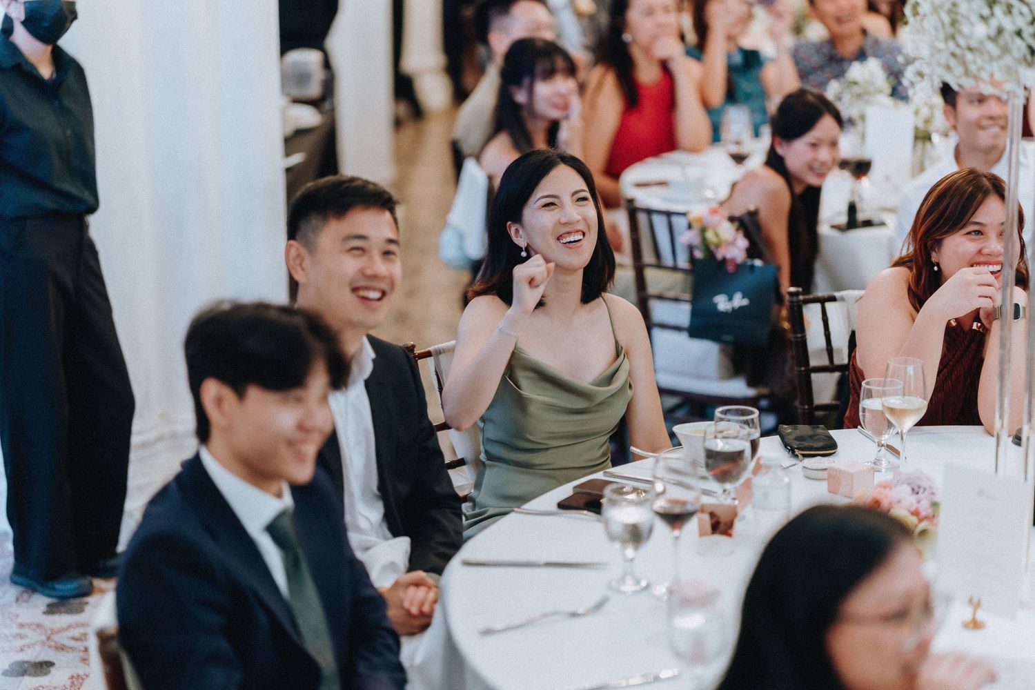 Wedding guests laugh and smile at reception dinner tables during celebration.