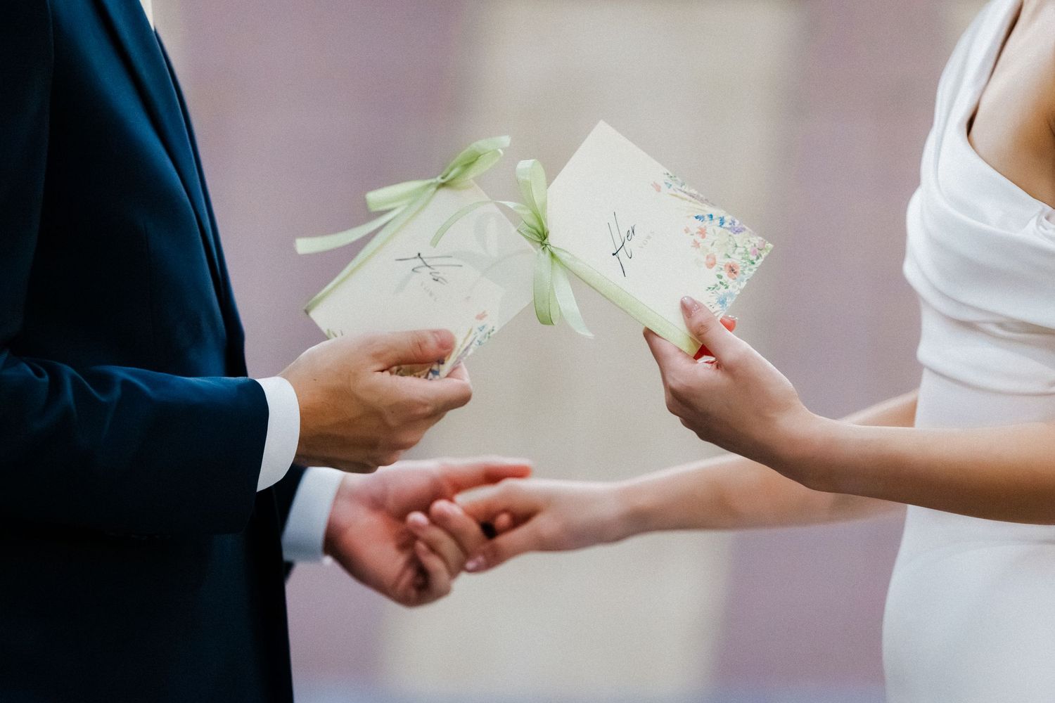 Bride and groom exchanging handwritten wedding vows cards tied with green ribbon during outdoor ceremony.