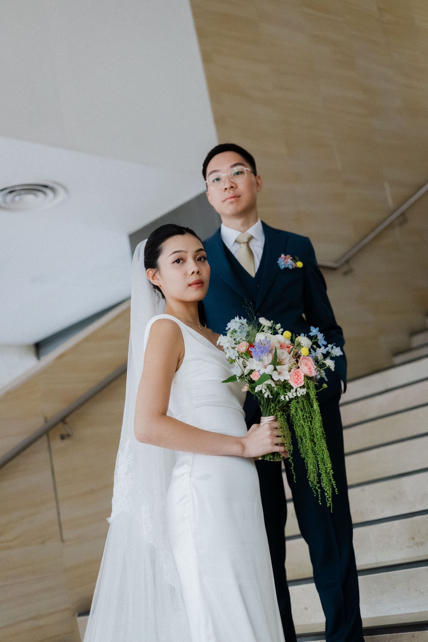 Asian bride and groom posing on staircase with colorful bridal bouquet.