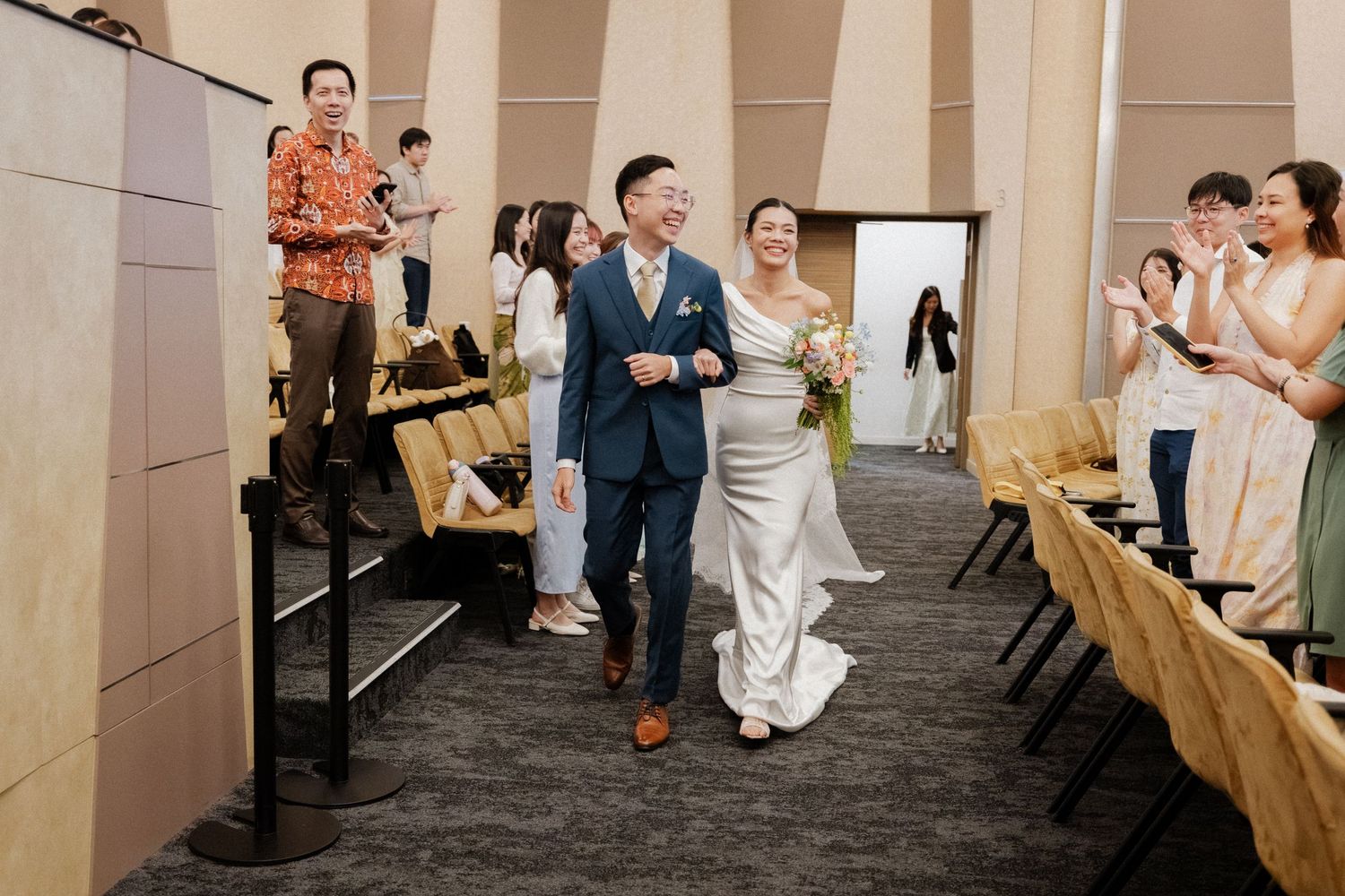 Newlywed couple walking joyfully down aisle as guests applaud at wedding ceremony recessional.