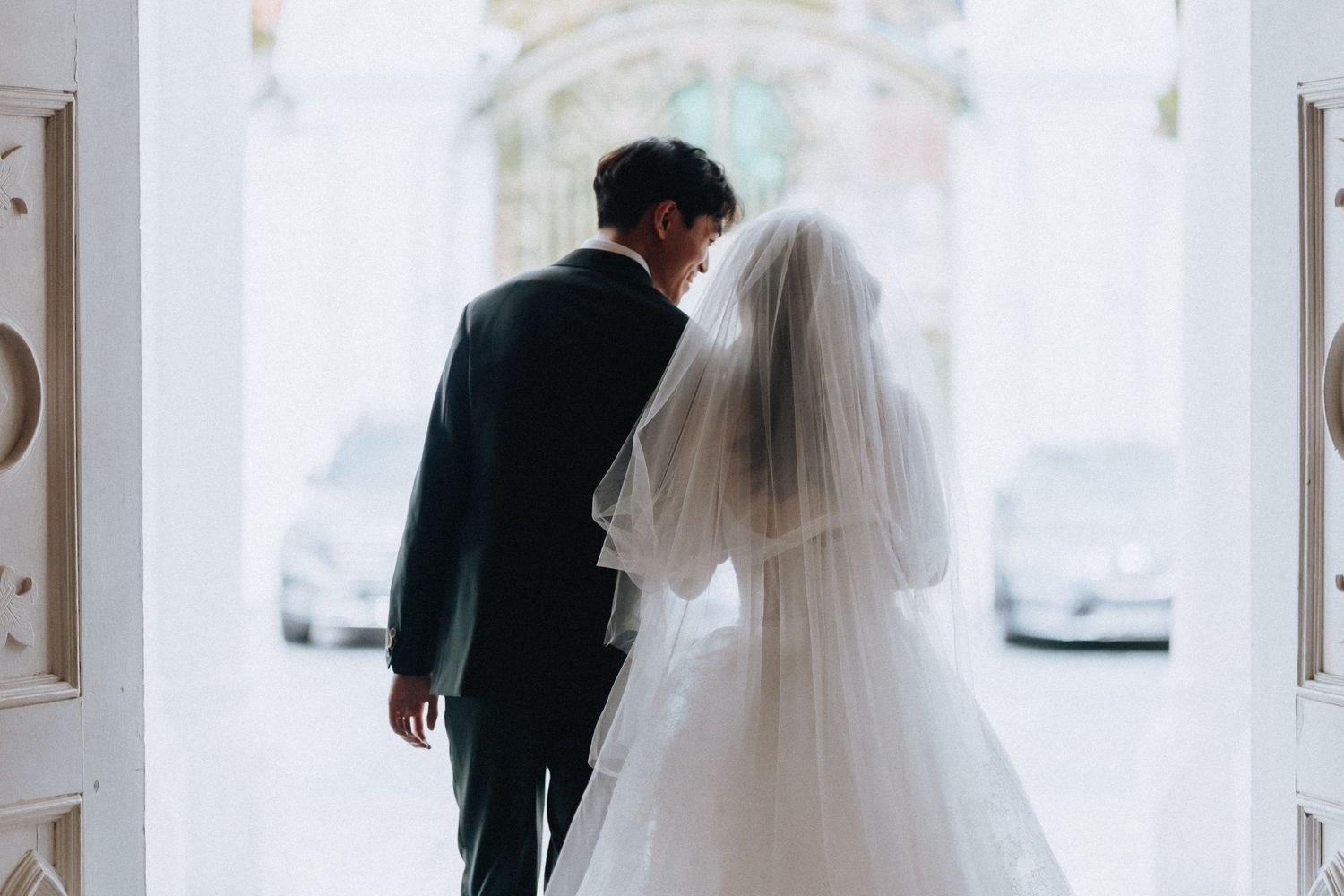 Bride and groom sharing a romantic moment at church doors, bride in white gown and veil, groom in dark suit.
