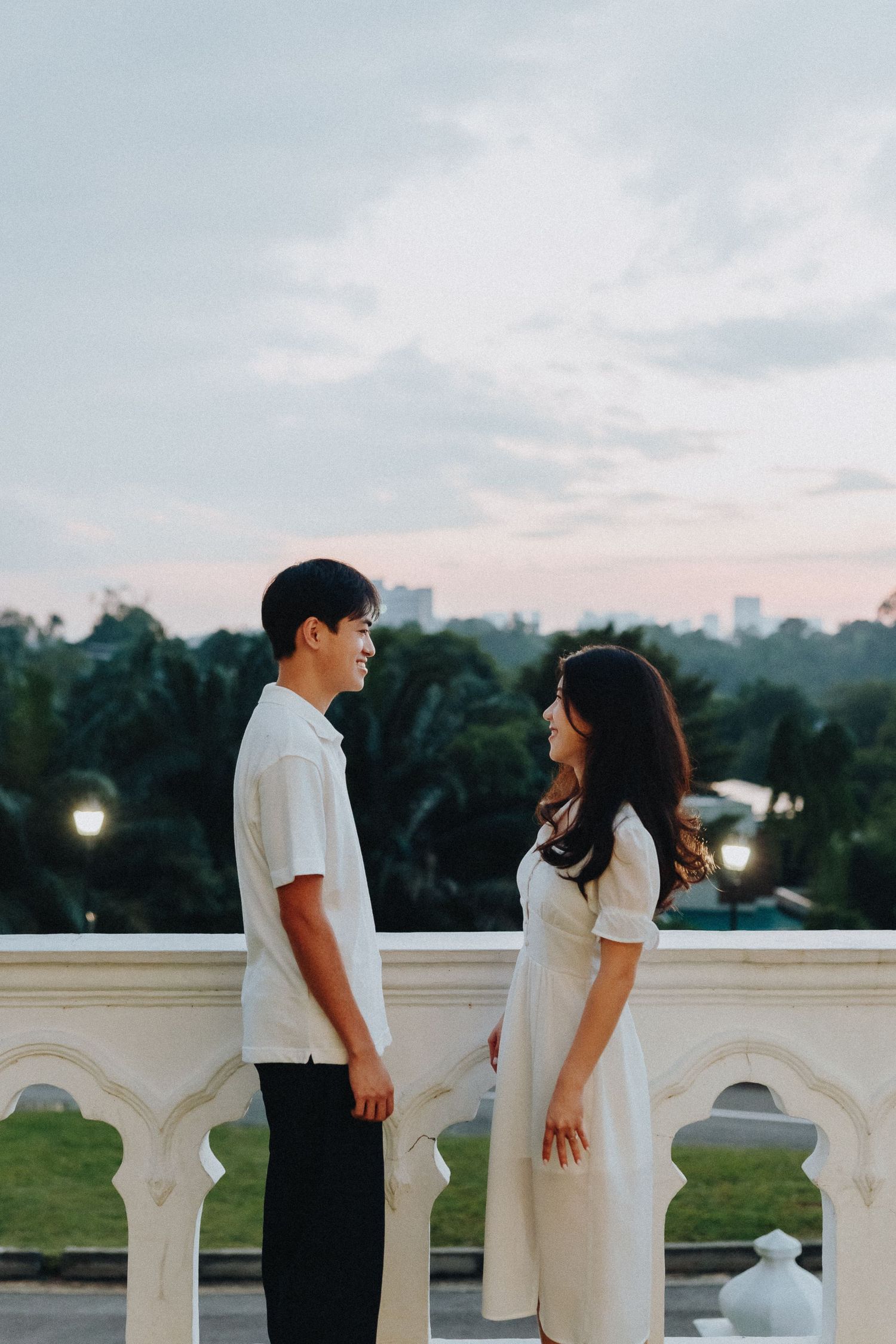 A couple in white shirts stands by a white balustrade at sunset creating a romantic silhouette.