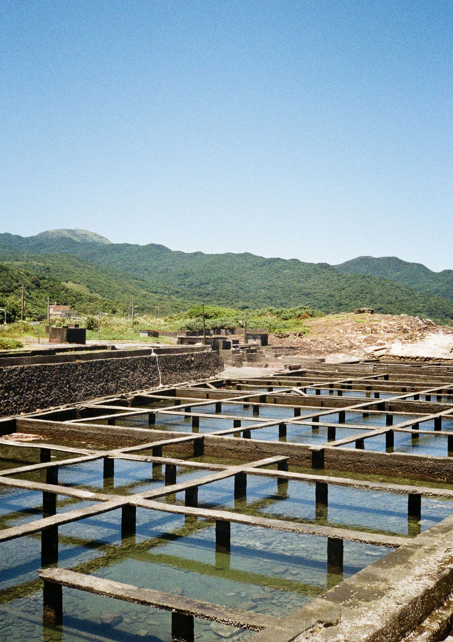 Geometric grid of water pools with wooden beams stretching across a salt farm with mountains in the background.