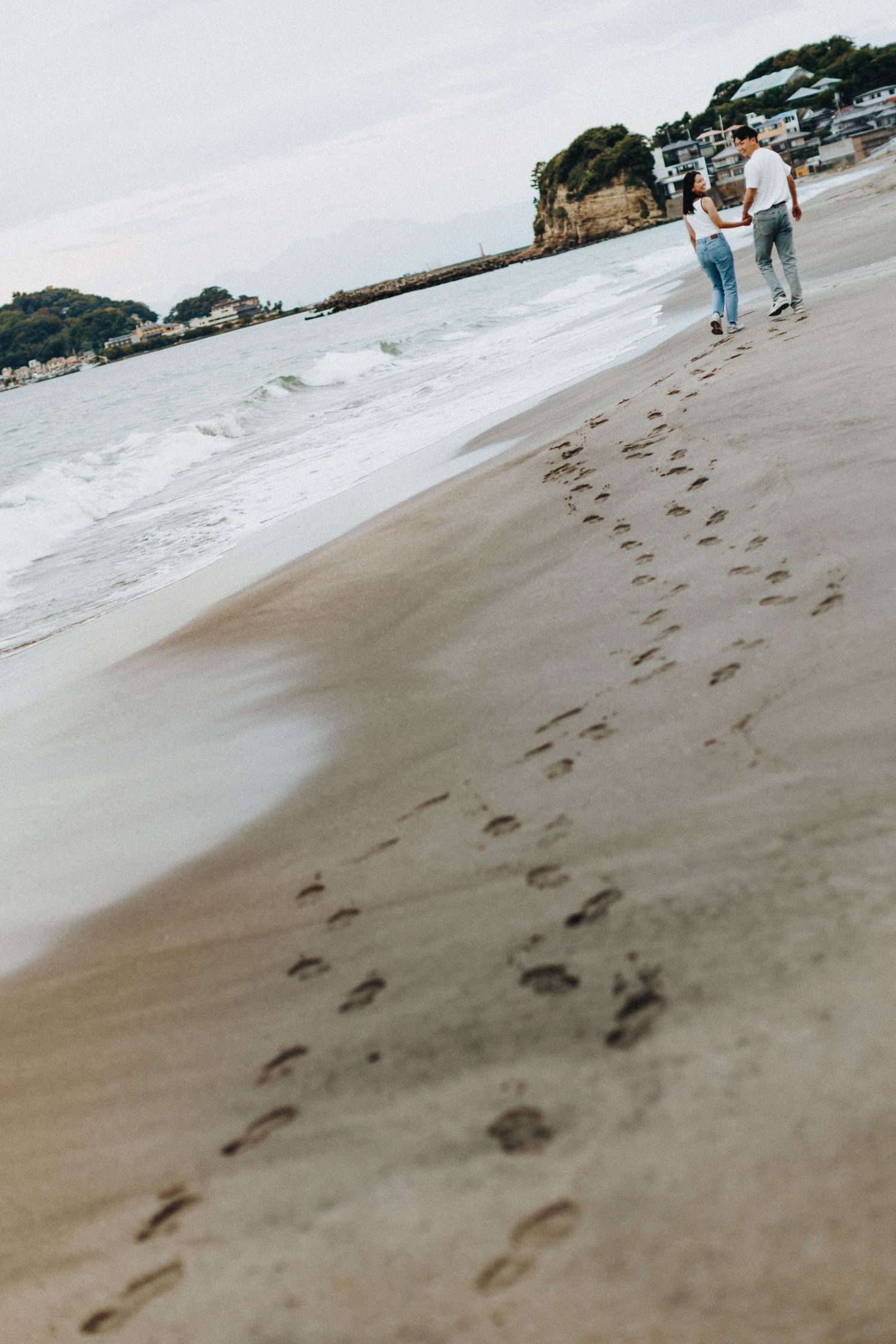 Trail of footprints in wet sand along a scenic beach shoreline.