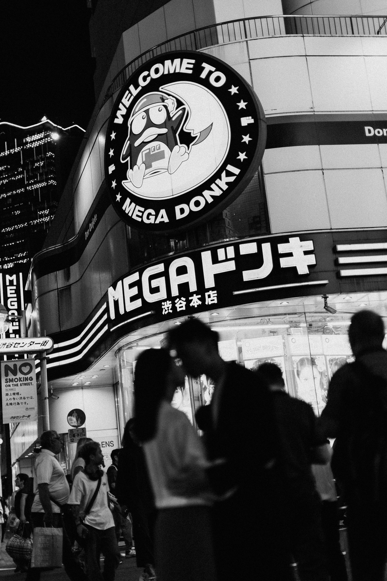 Black and white urban nightscape with neon signs and silhouetted crowd.