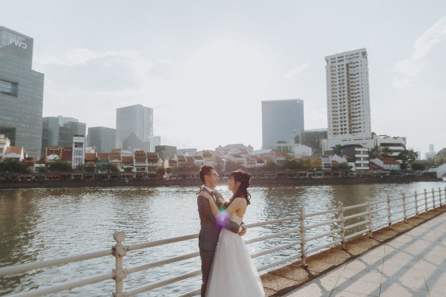 Wedding couple poses along waterfront with city skyline and tall buildings in background.