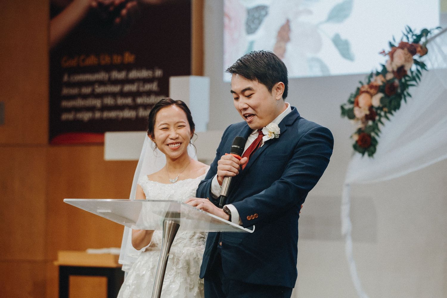 A couple shares a joyful moment at a wedding ceremony podium while giving speeches.