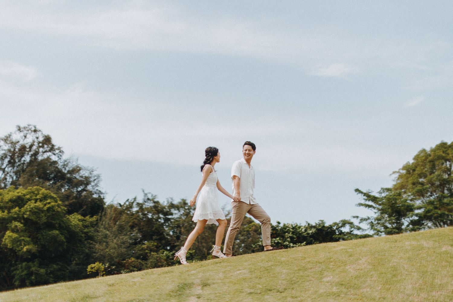 A couple walking together on a grassy hilltop against a bright blue sky.
