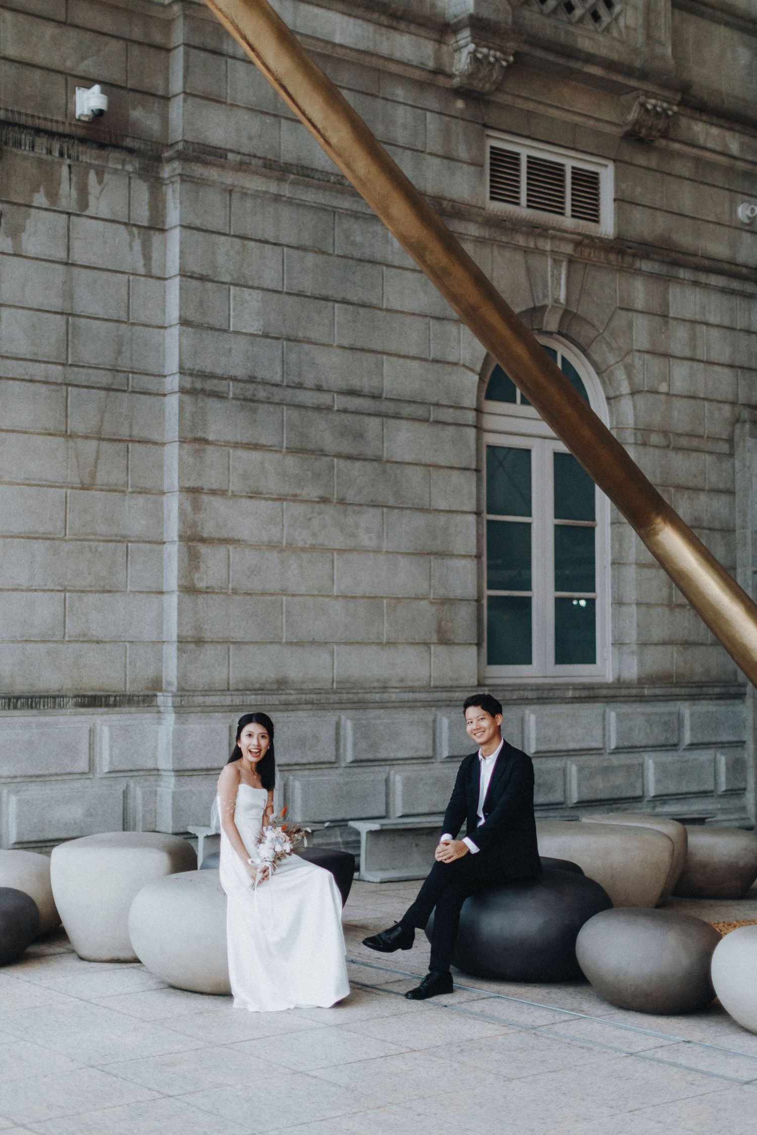 An elegant couple sits on modern stone seating against a classic architectural backdrop.