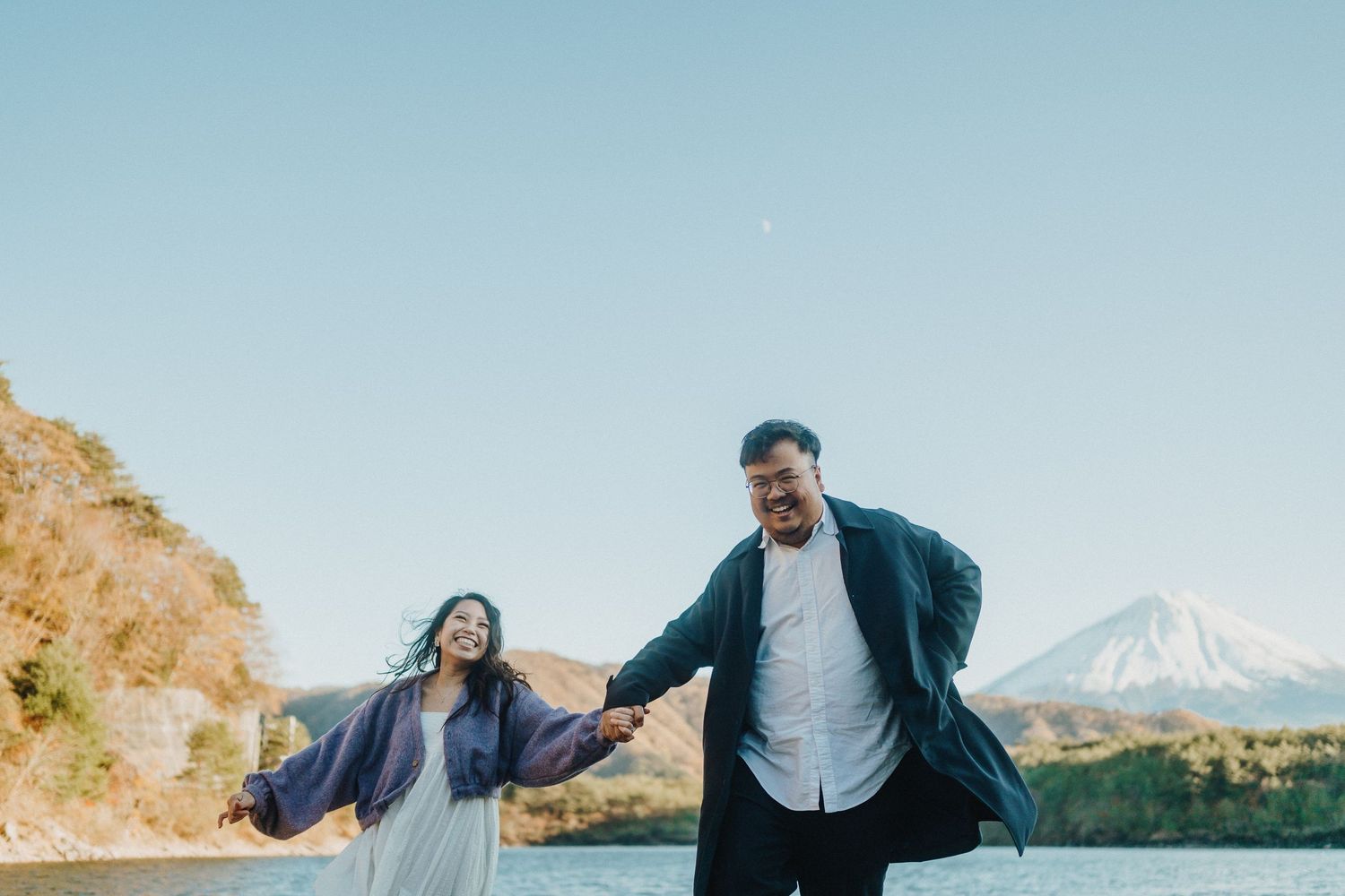A couple shares a playful moment on a mountain path with a snow-capped peak in the distance.