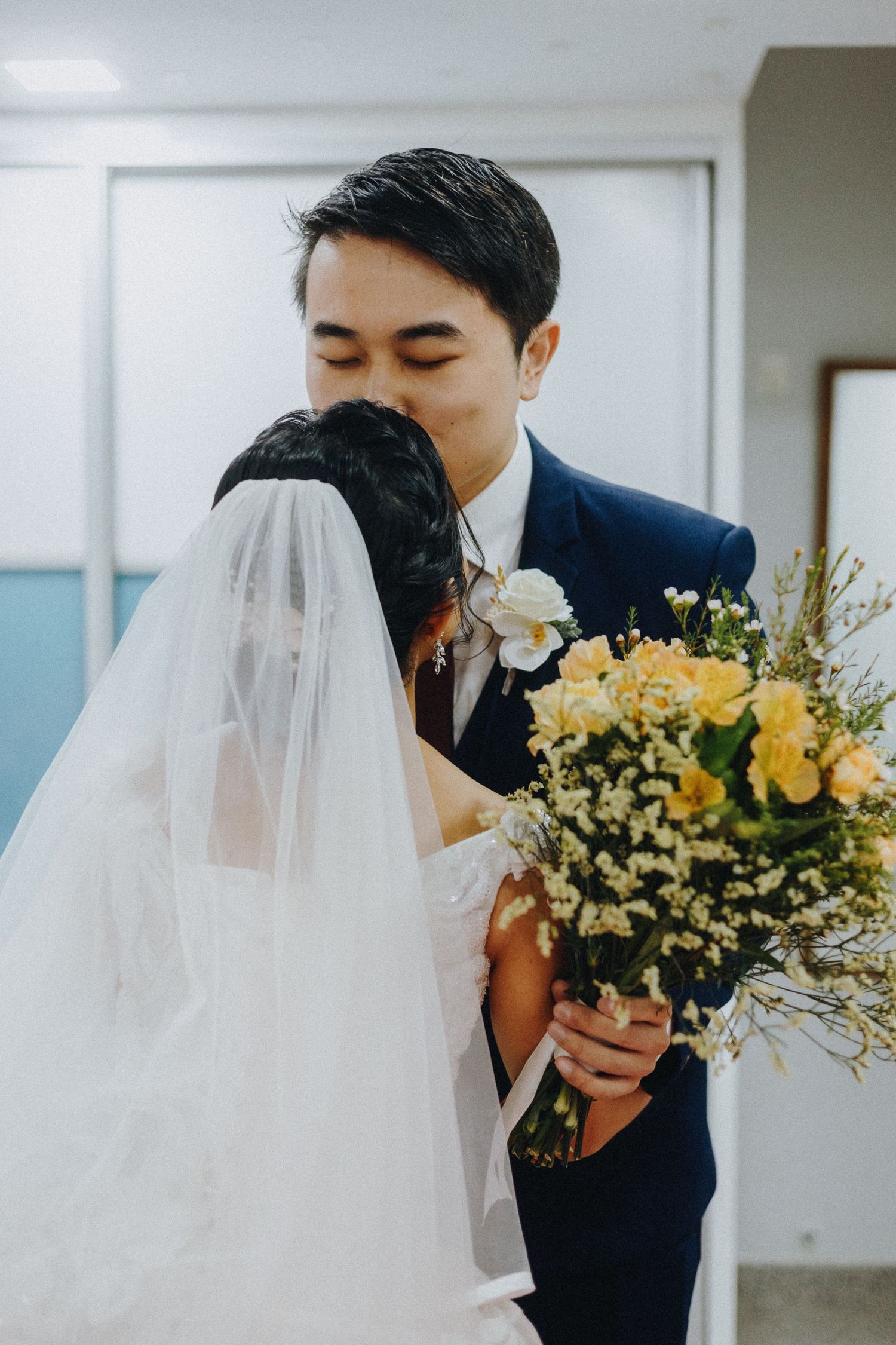 A tender wedding moment as a couple shares a kiss while the bride holds a beautiful yellow and white floral bouquet.