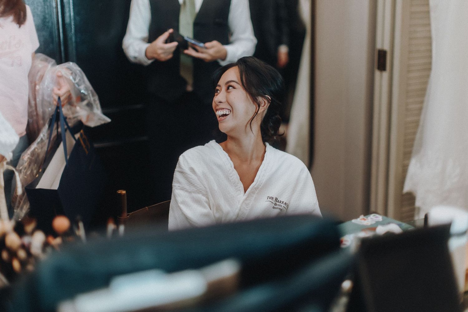 A wedding party member receives makeup application in preparation for the ceremony in a hotel room.