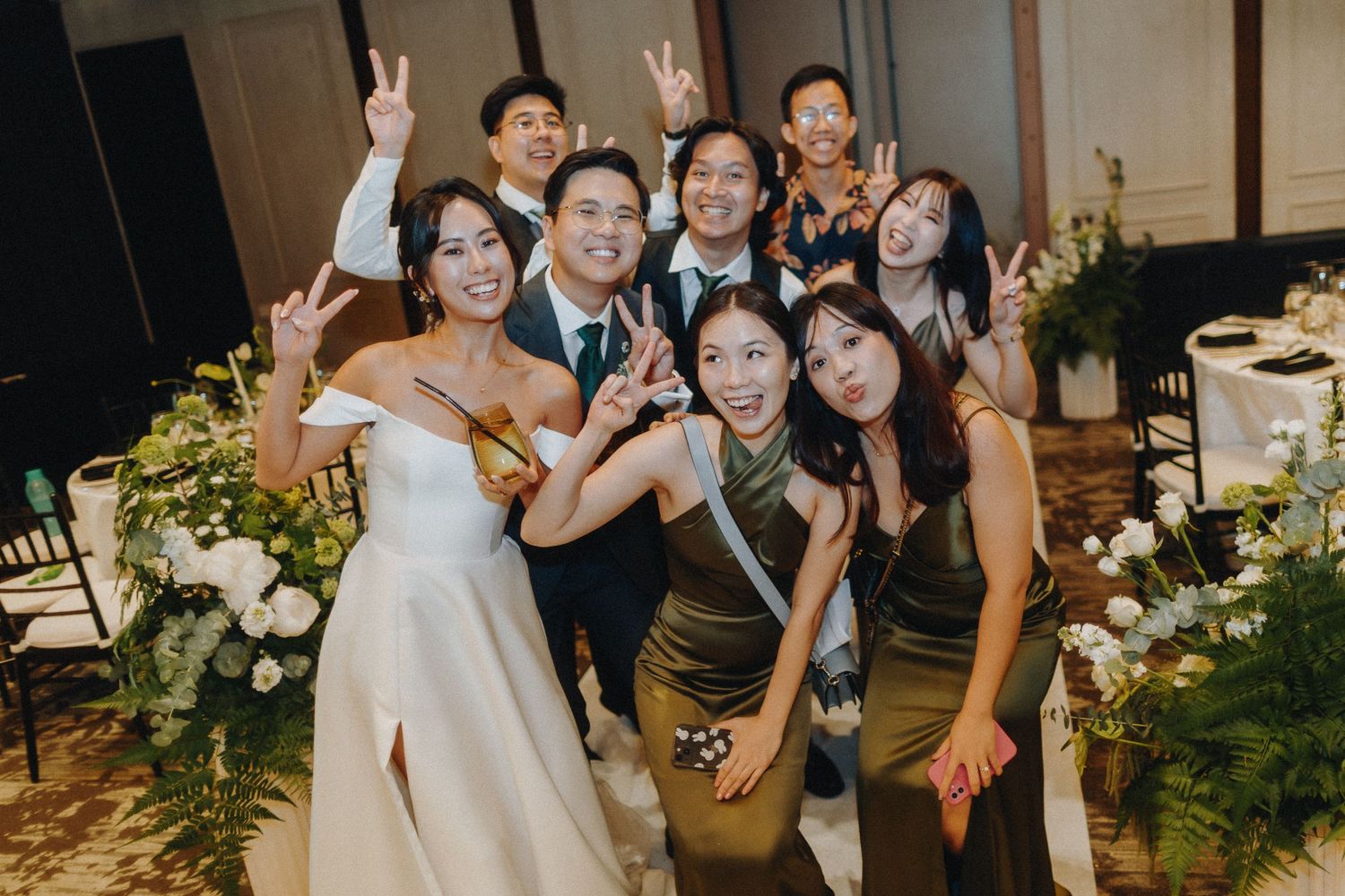 Wedding celebration with guests posing and making peace signs during a lively reception party.