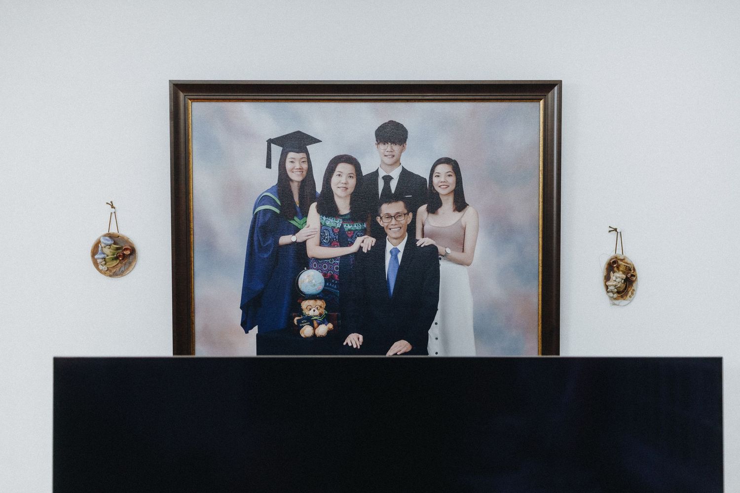 A formal family portrait in a dark wooden frame hangs on a light grey wall between two wall sconces.