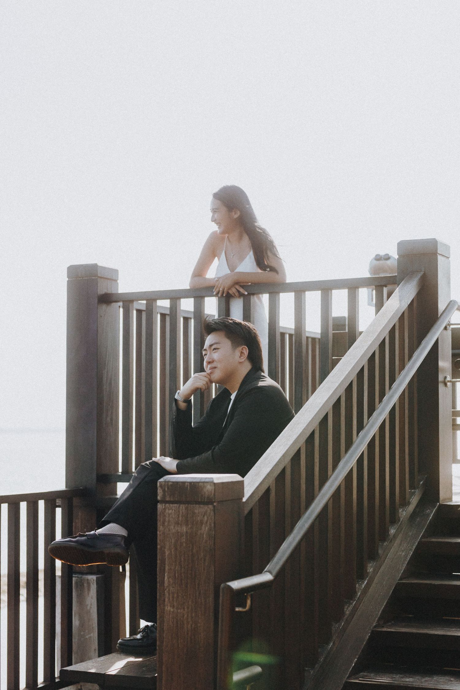 People sitting on wooden steps of an outdoor viewing platform on a misty day.