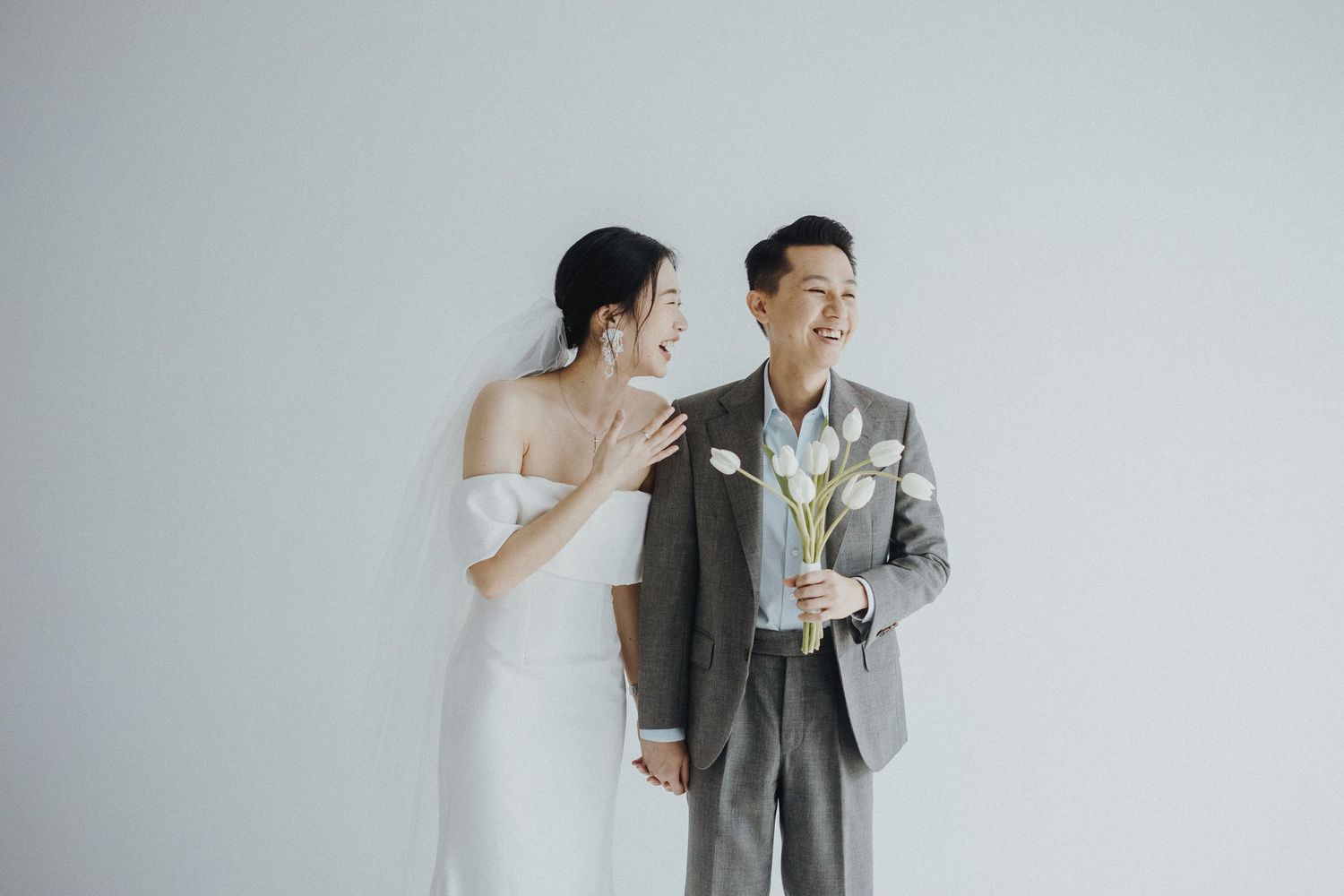 Bride and groom share a lighthearted moment while dancing in a minimalist studio setting.