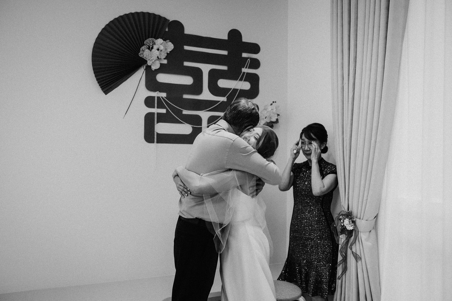 A celebration scene in a minimalist room with a black decorative fan and Chinese double happiness symbol on wall.