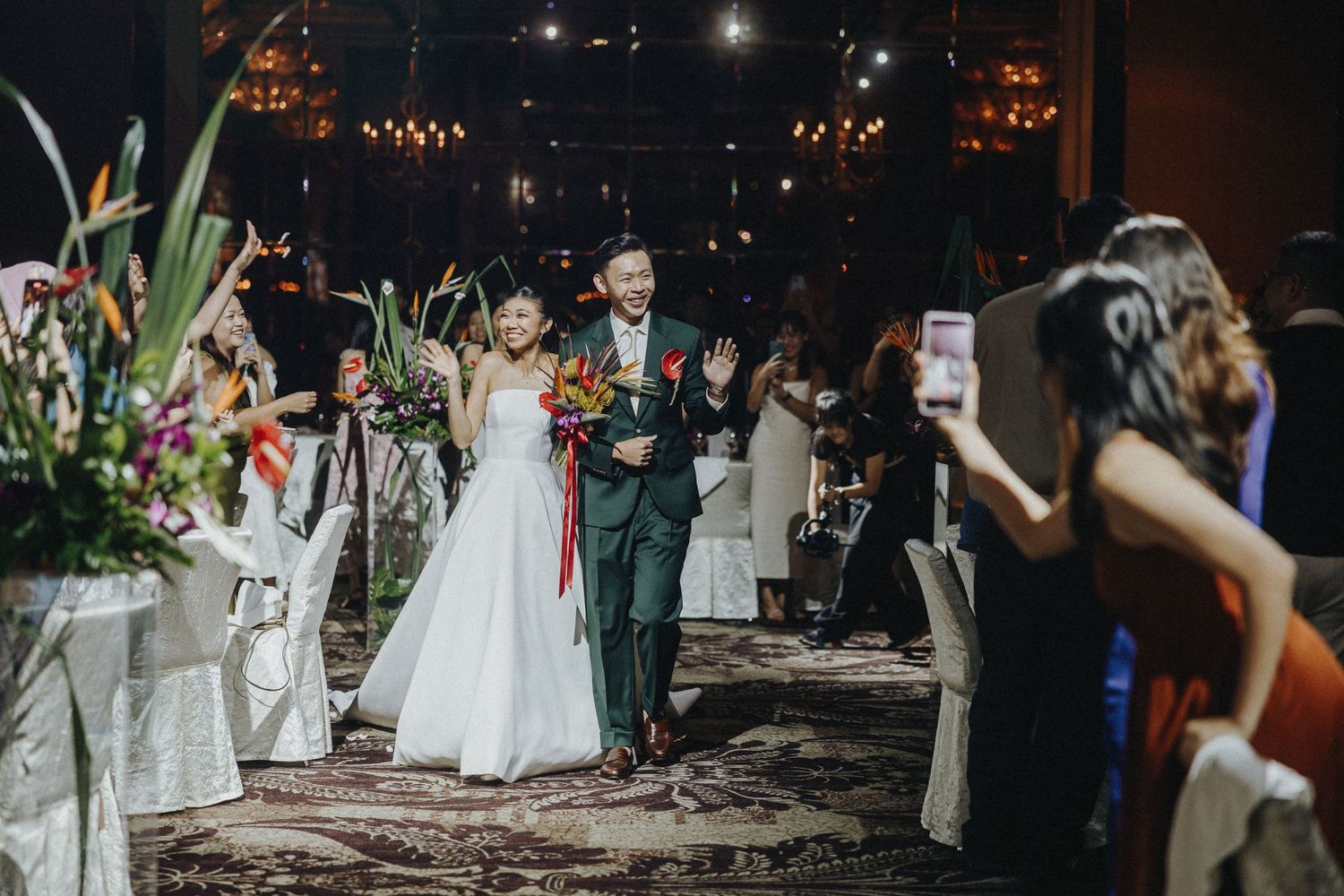 A wedding celebration in a dimly lit venue with guests capturing photos on their phones.