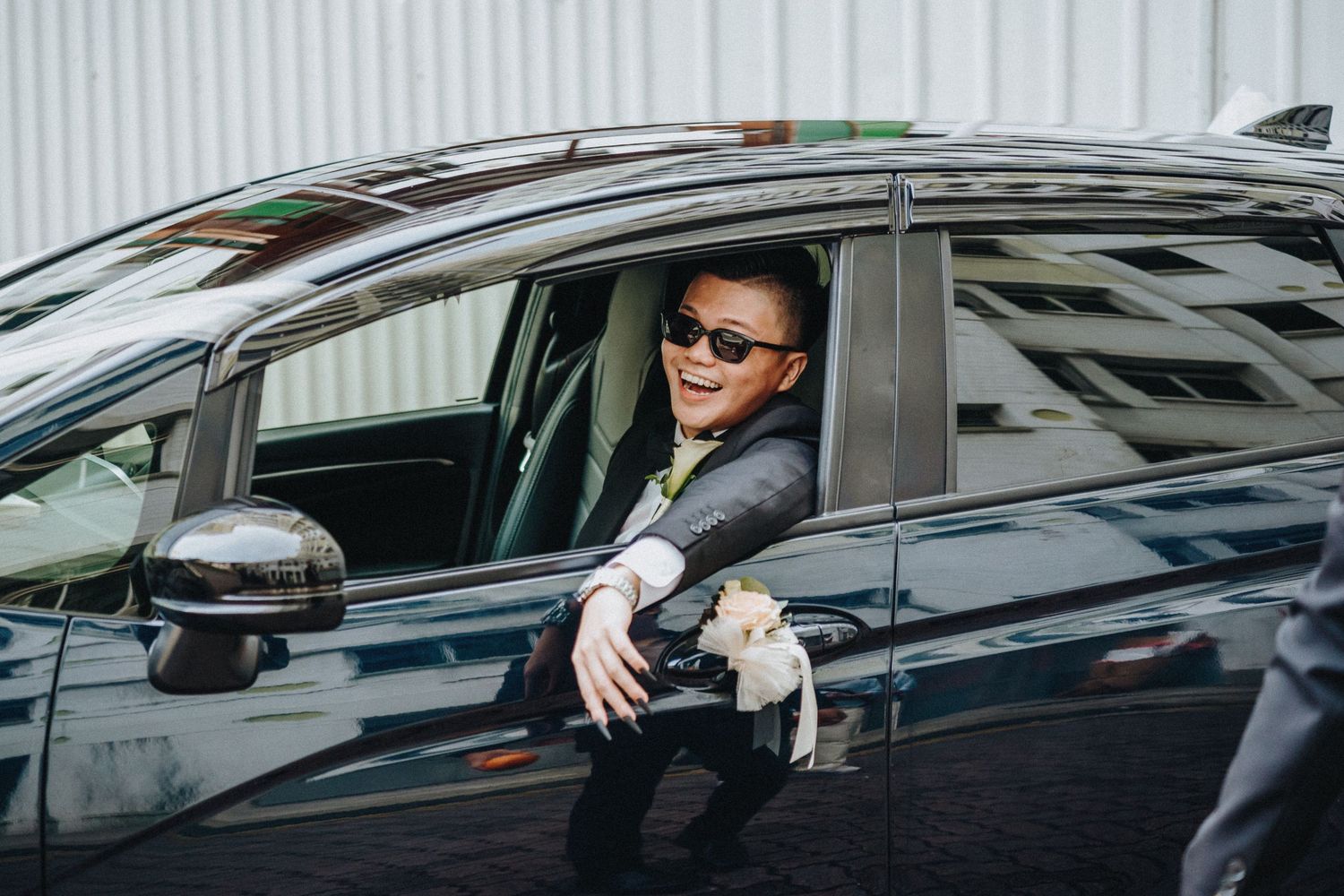 Person in dark suit exits black luxury sedan vehicle while placing hand inside jacket pocket.