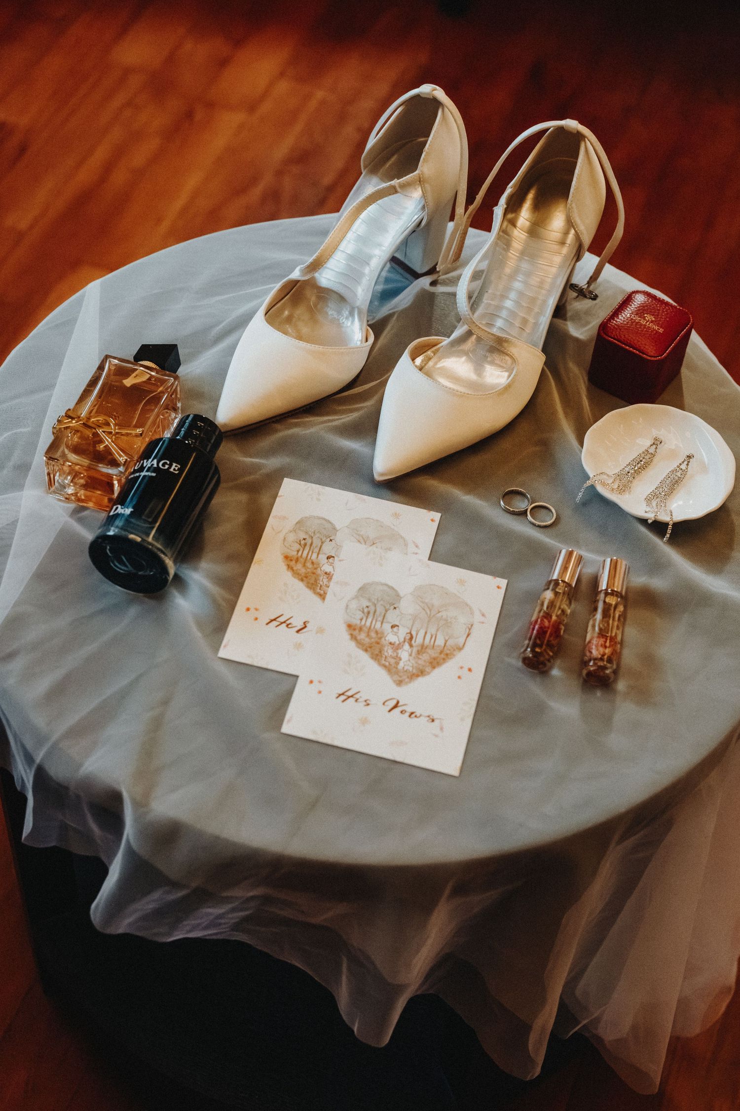 Wedding accessories including white heels, rings, and invitation cards arranged on a gray surface.