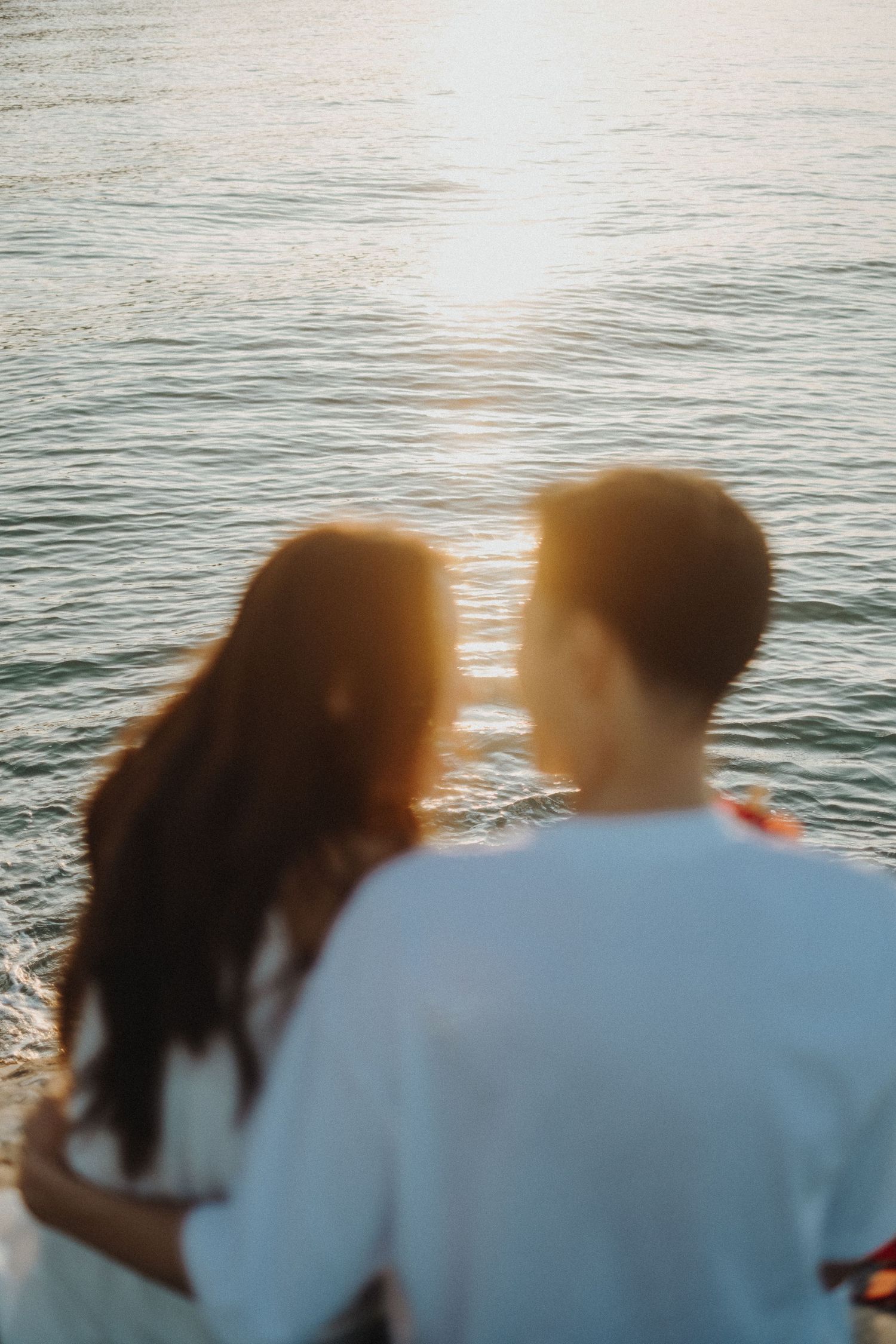 Silhouette of two people sitting close together against the ocean at sunset.