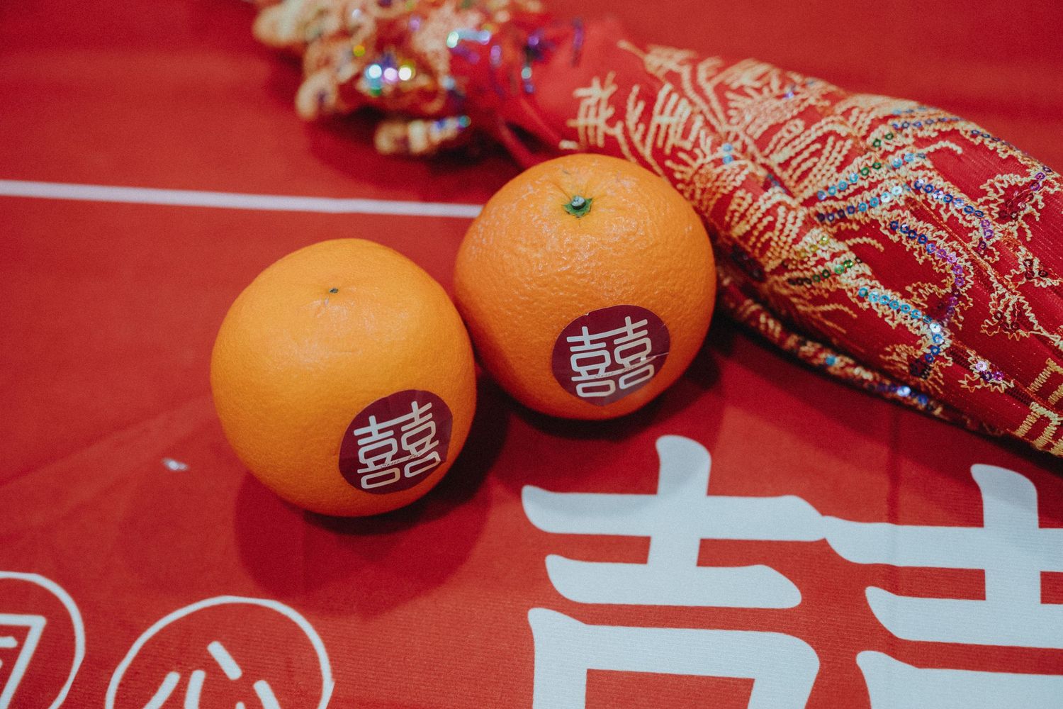 Fresh oranges with Chinese New Year stickers and traditional red decorations on a festive red background.