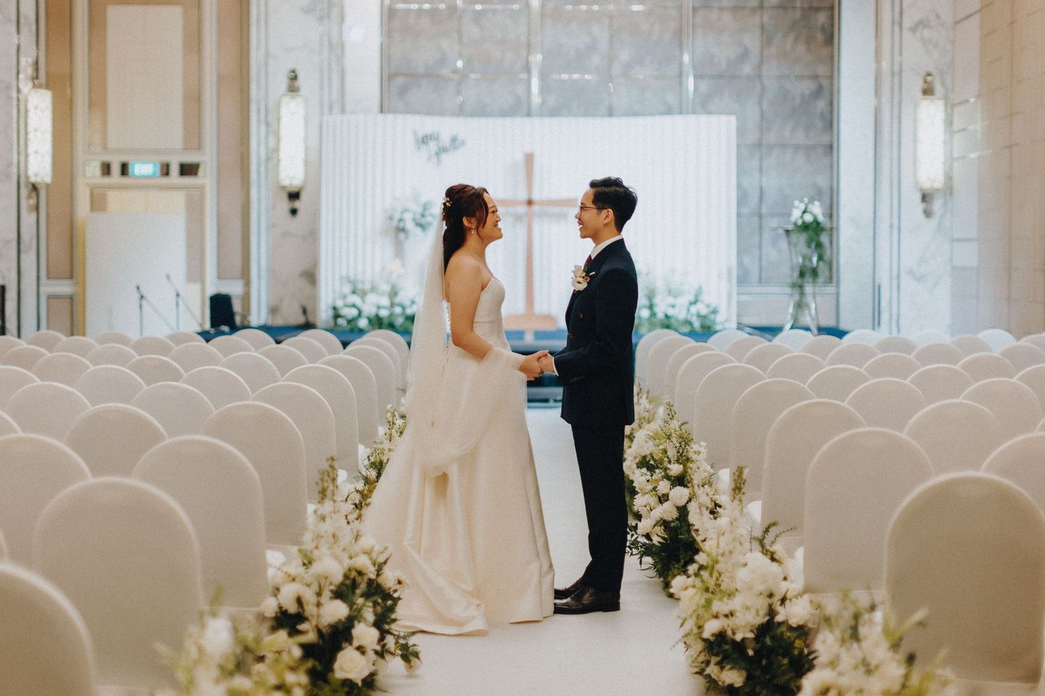 An elegant wedding venue decorated with white chairs and floral arrangements along the aisle.
