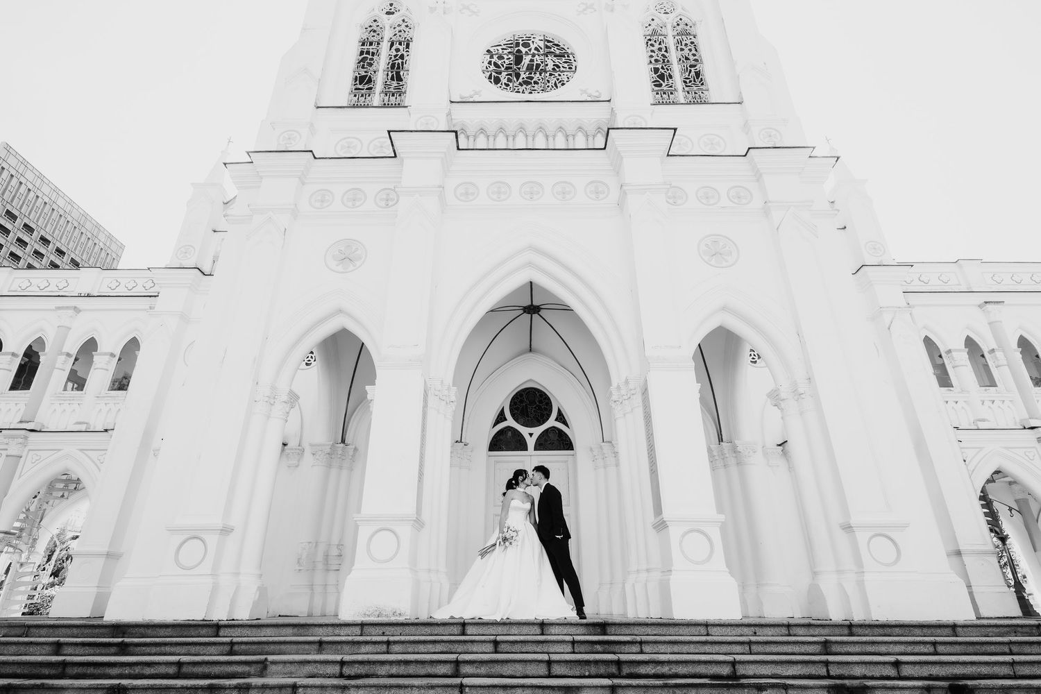 Bride and groom embracing on the steps of a stunning white Gothic cathedral.