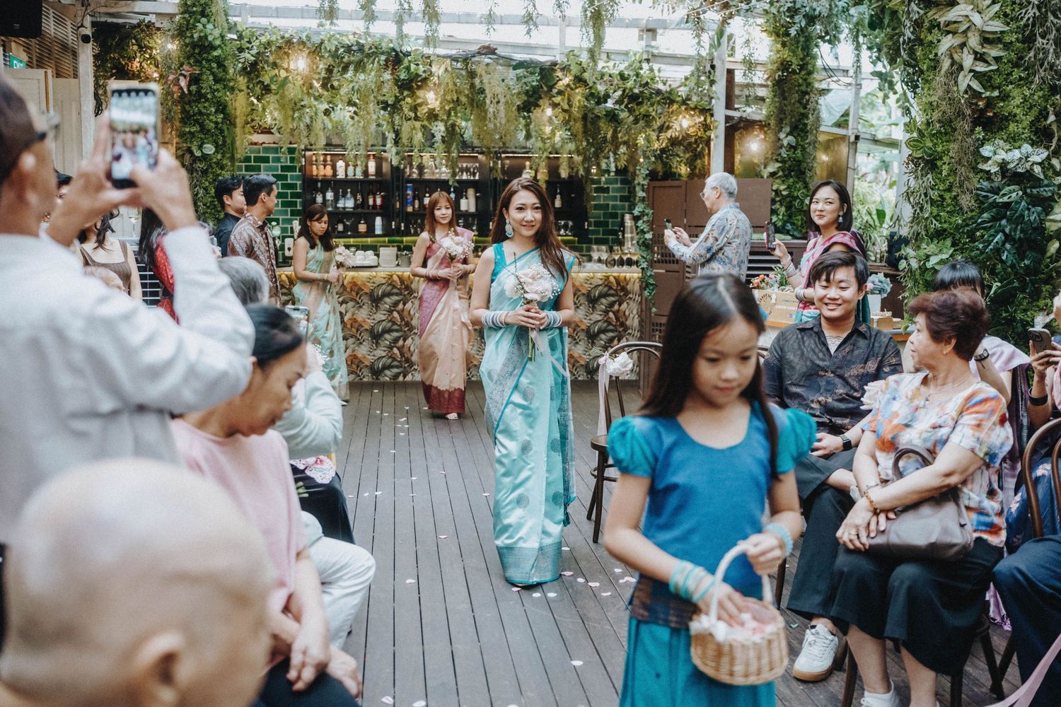 Women in traditional ao dai gowns walk through a lush greenhouse venue during an elegant cultural ceremony.