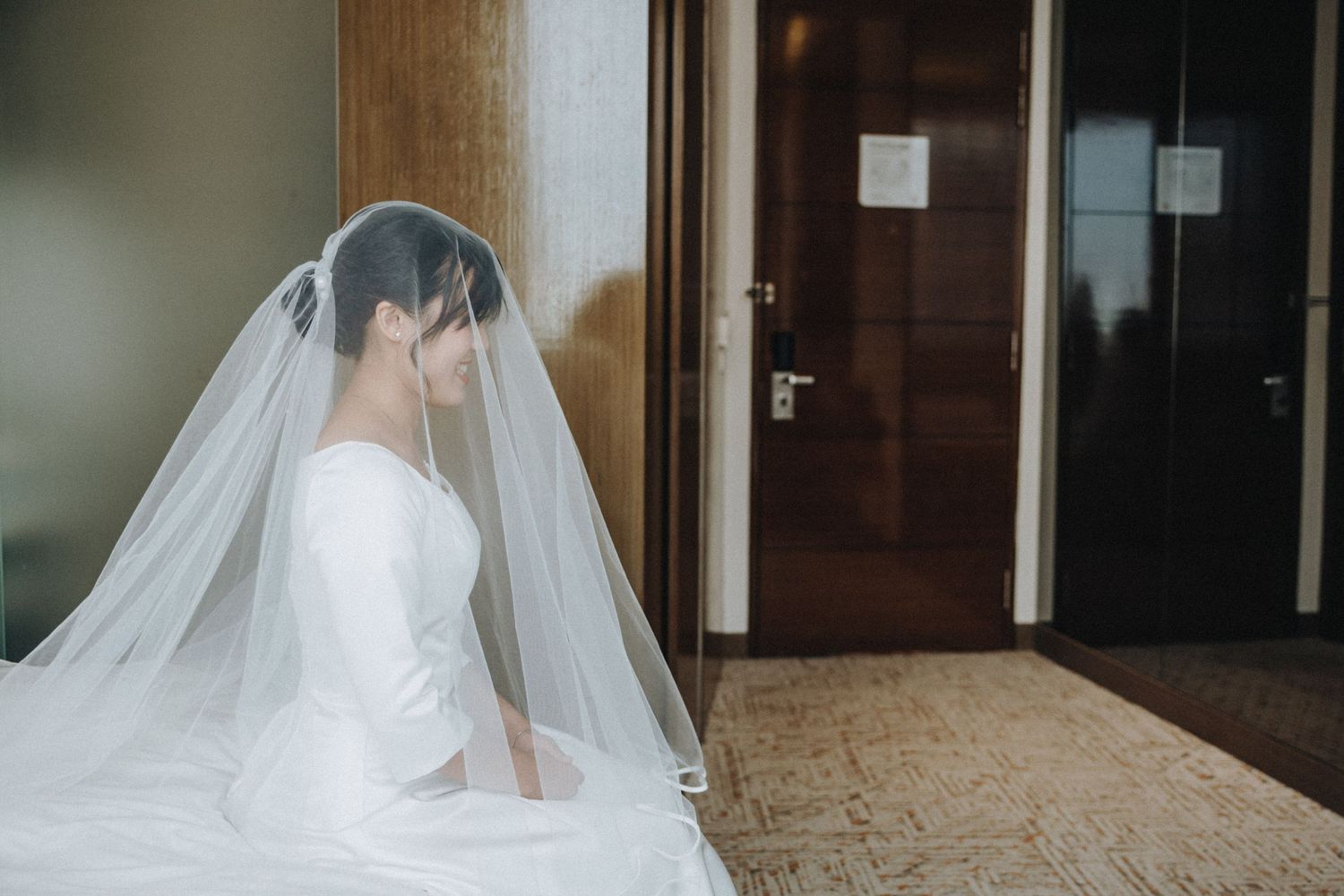 Bride in white gown and veil sitting quietly before wedding ceremony.