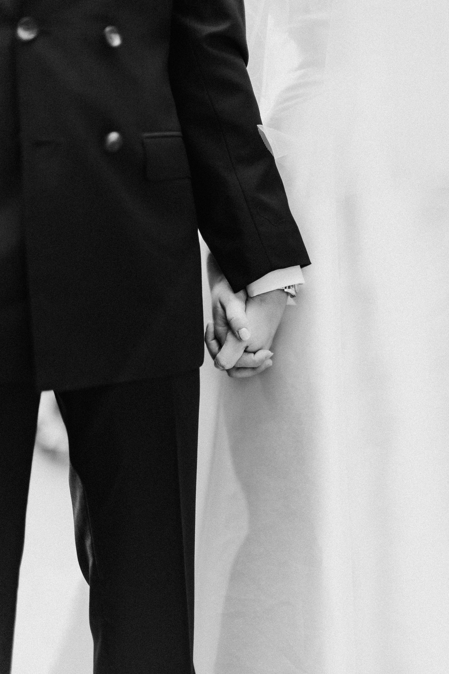 Black and white close-up of formal wedding attire showing suit jackets and a white dress.