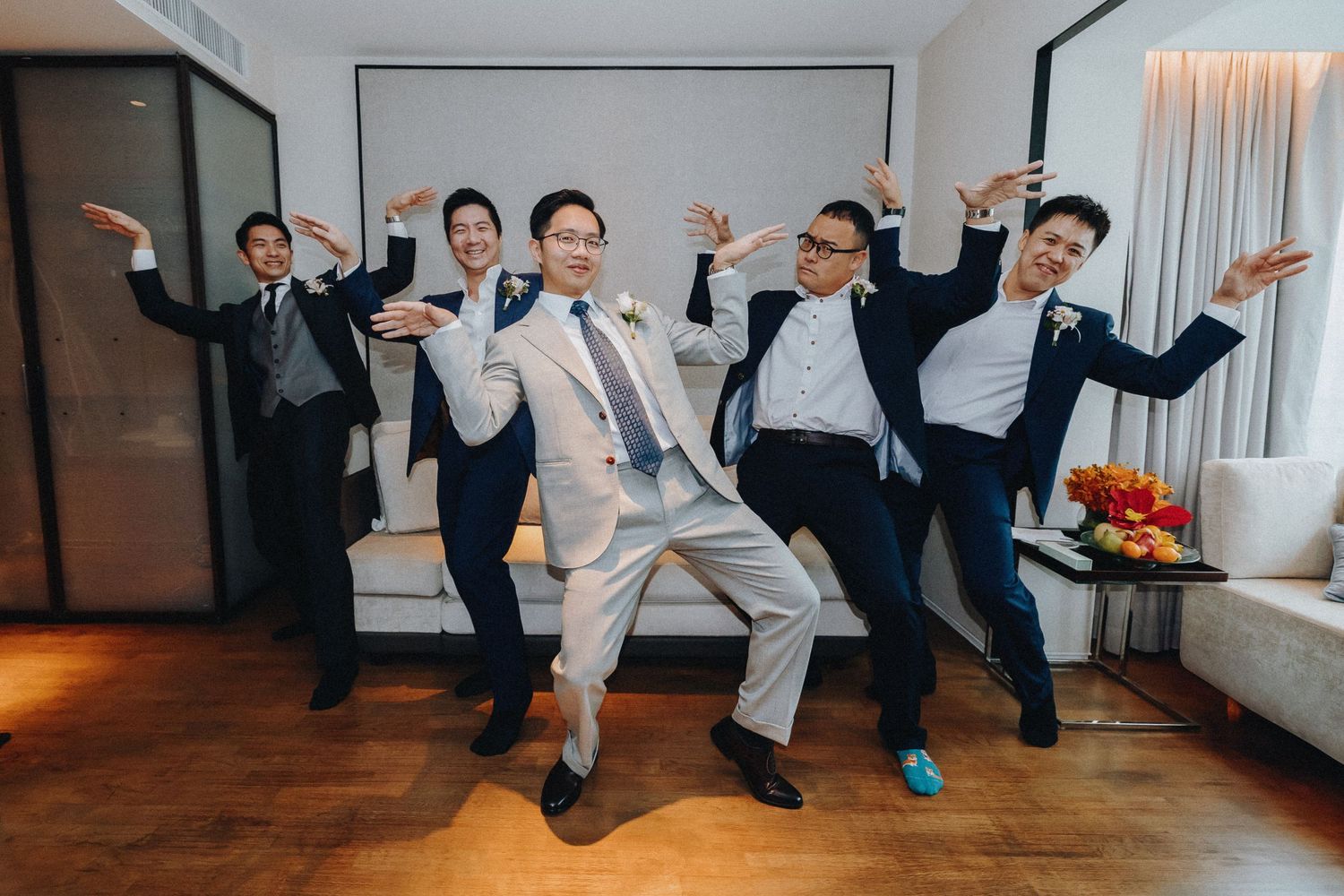 Wedding party members perform synchronized jumping poses on a wooden dance floor.