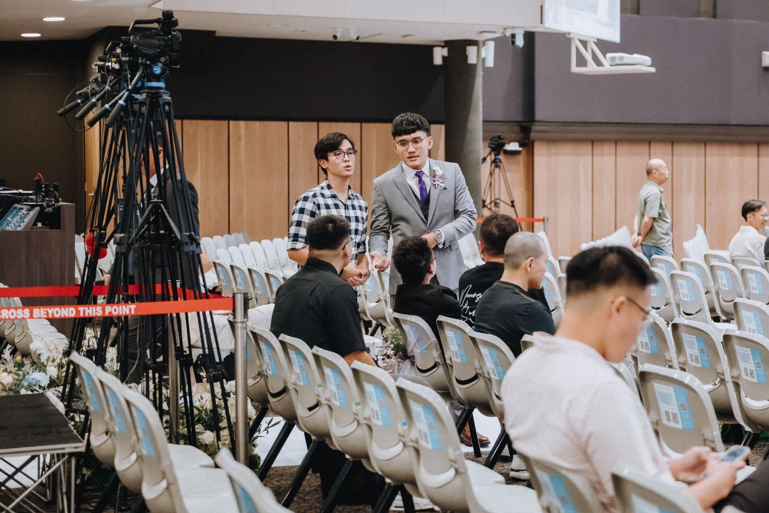 Professional camera equipment set up in an auditorium with scattered attendees in chairs.